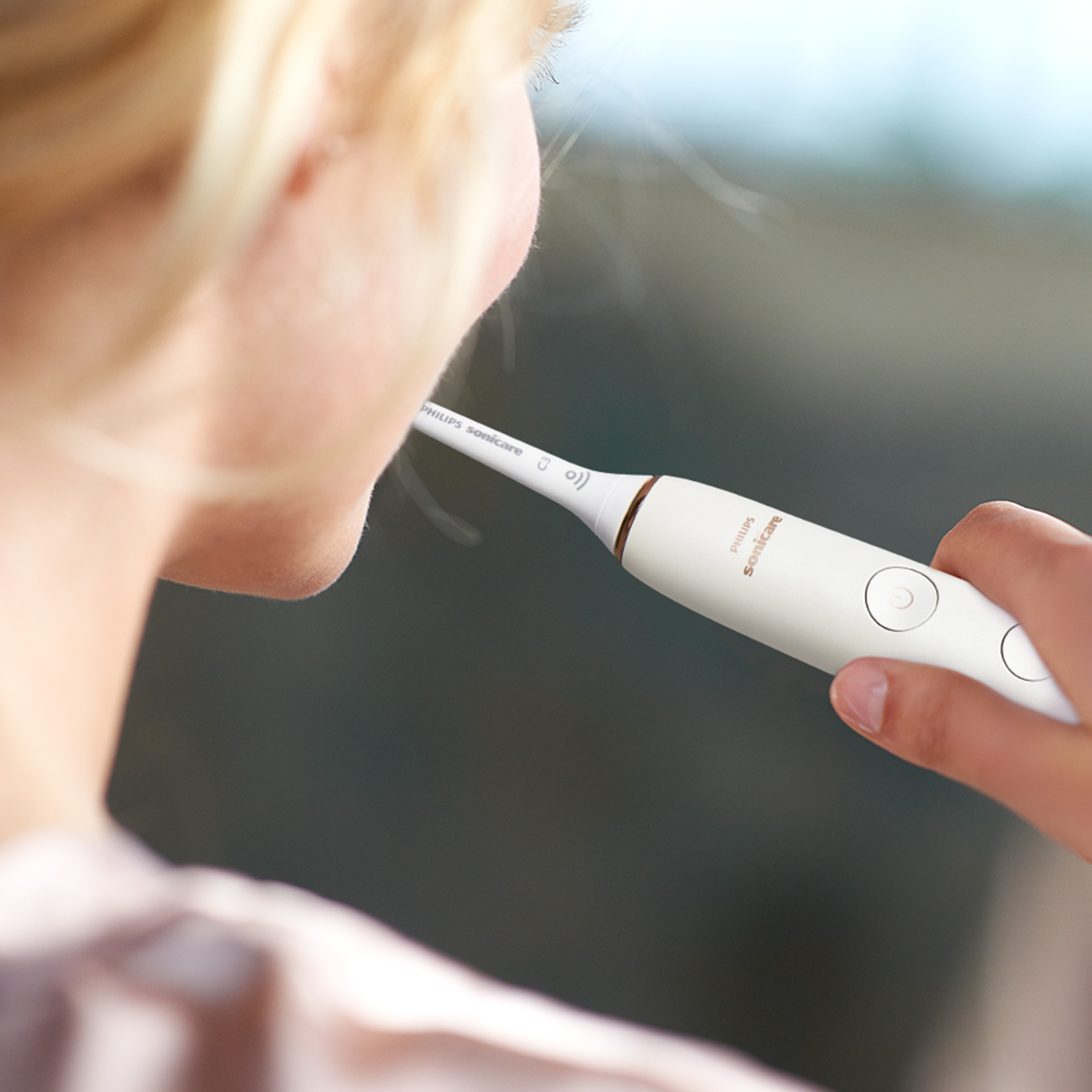 Kobieta myjąca zęby białą elektryczną szczoteczką do zębów.