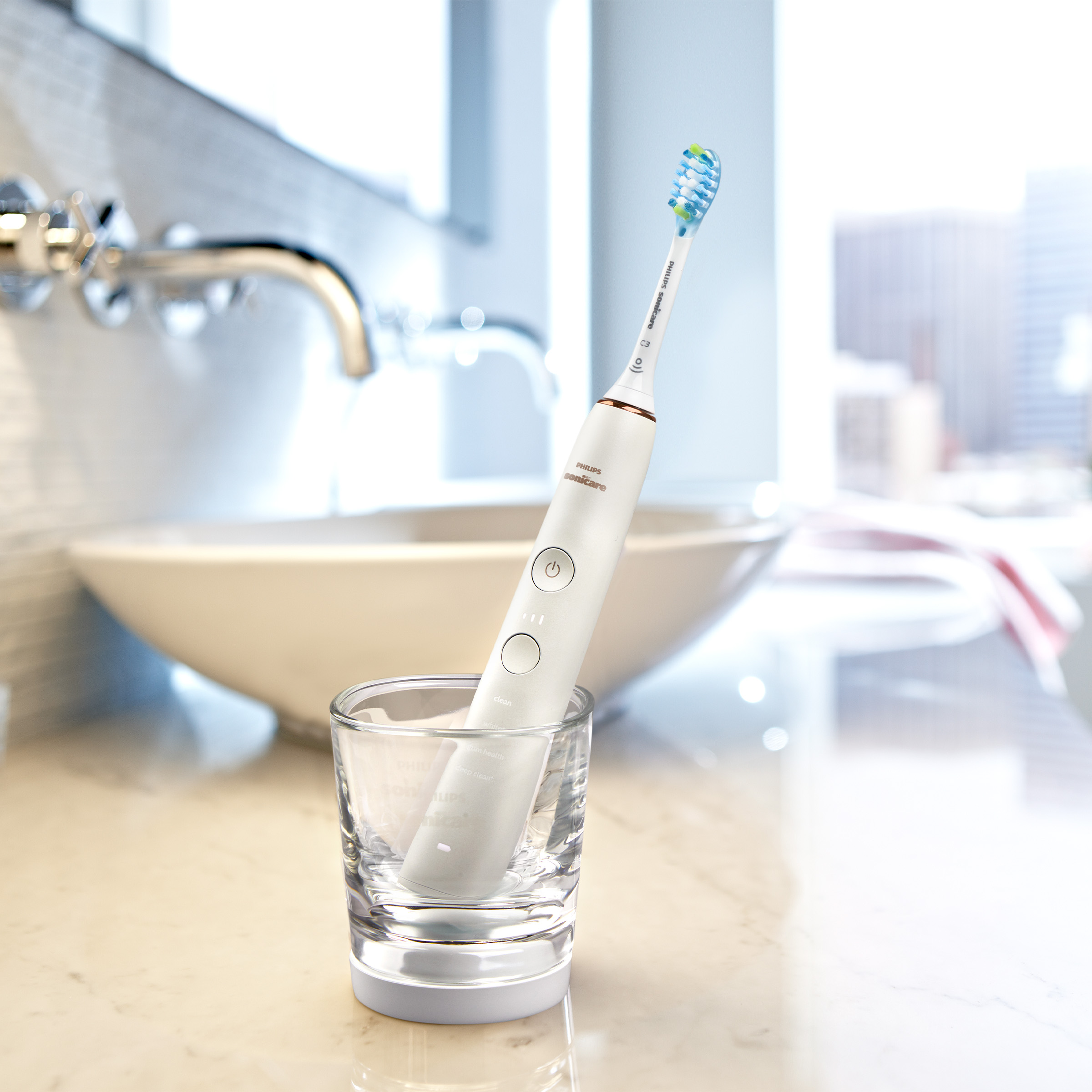 Elektryczna szczoteczka do zębów w szklance na marmurowej powierzchni.