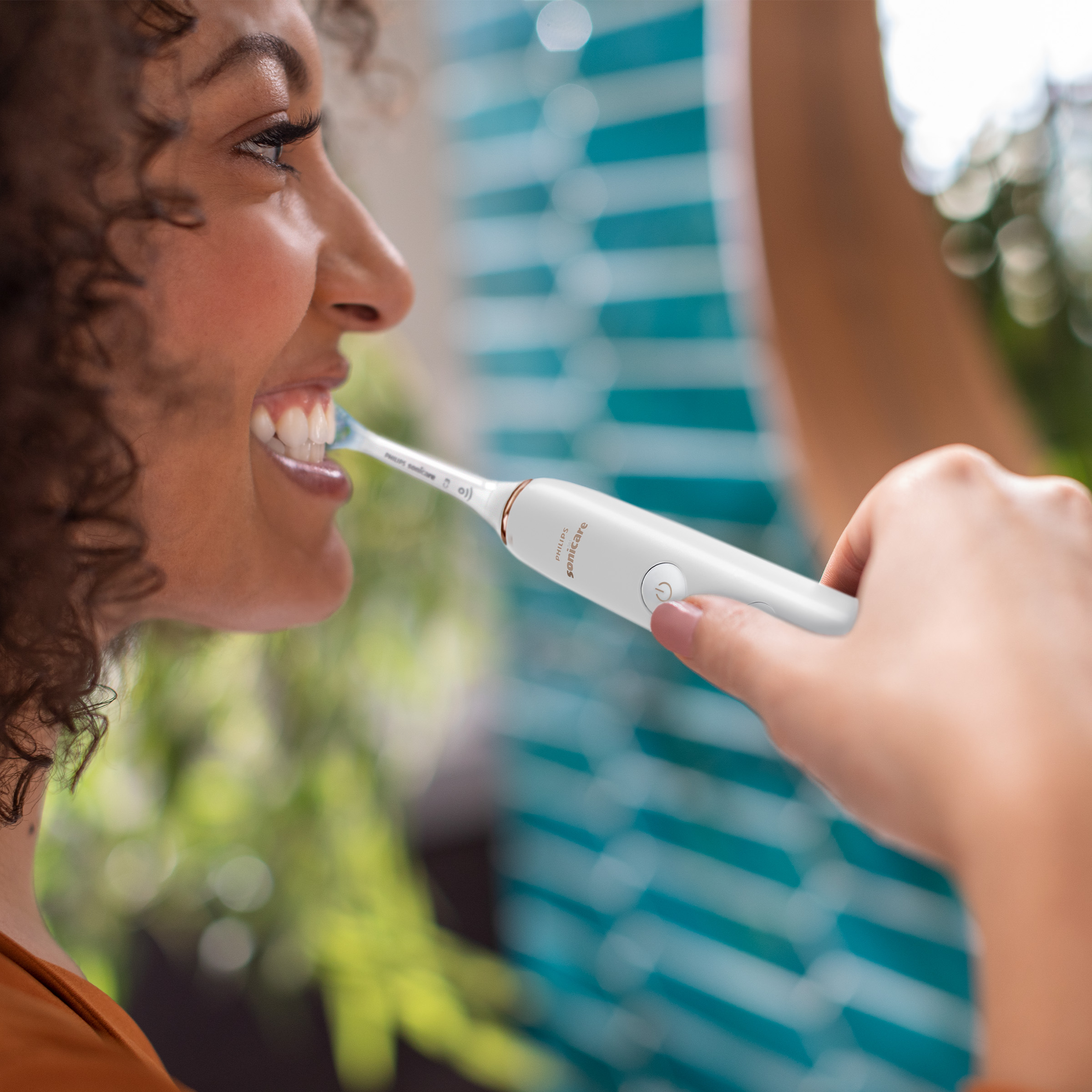 Kobieta myje zęby biało-złotą szczoteczką. Druga osoba jest poza ostrością.