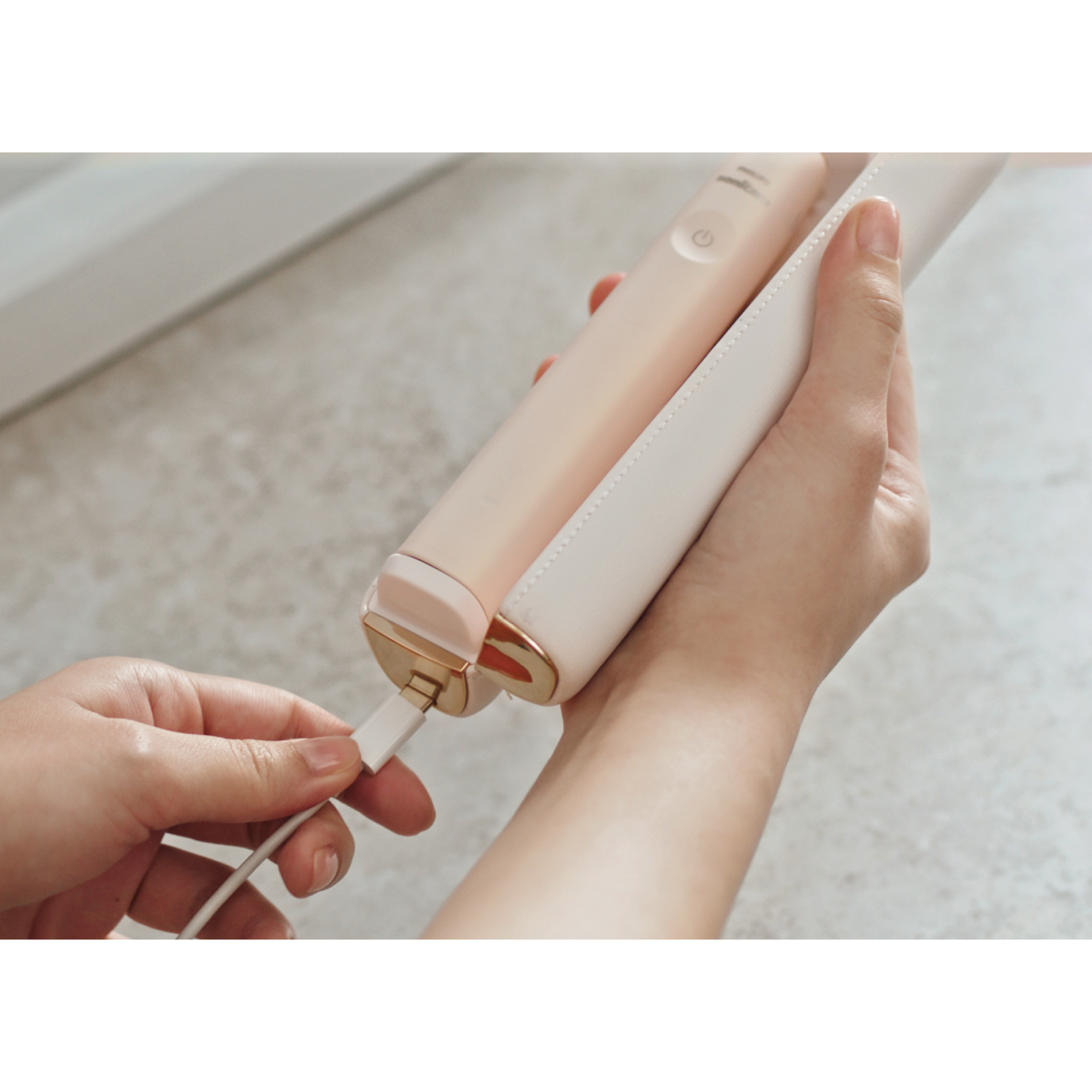 Osoba podłączająca kabel ładujący do białej elektrycznej szczoteczki do zębów.