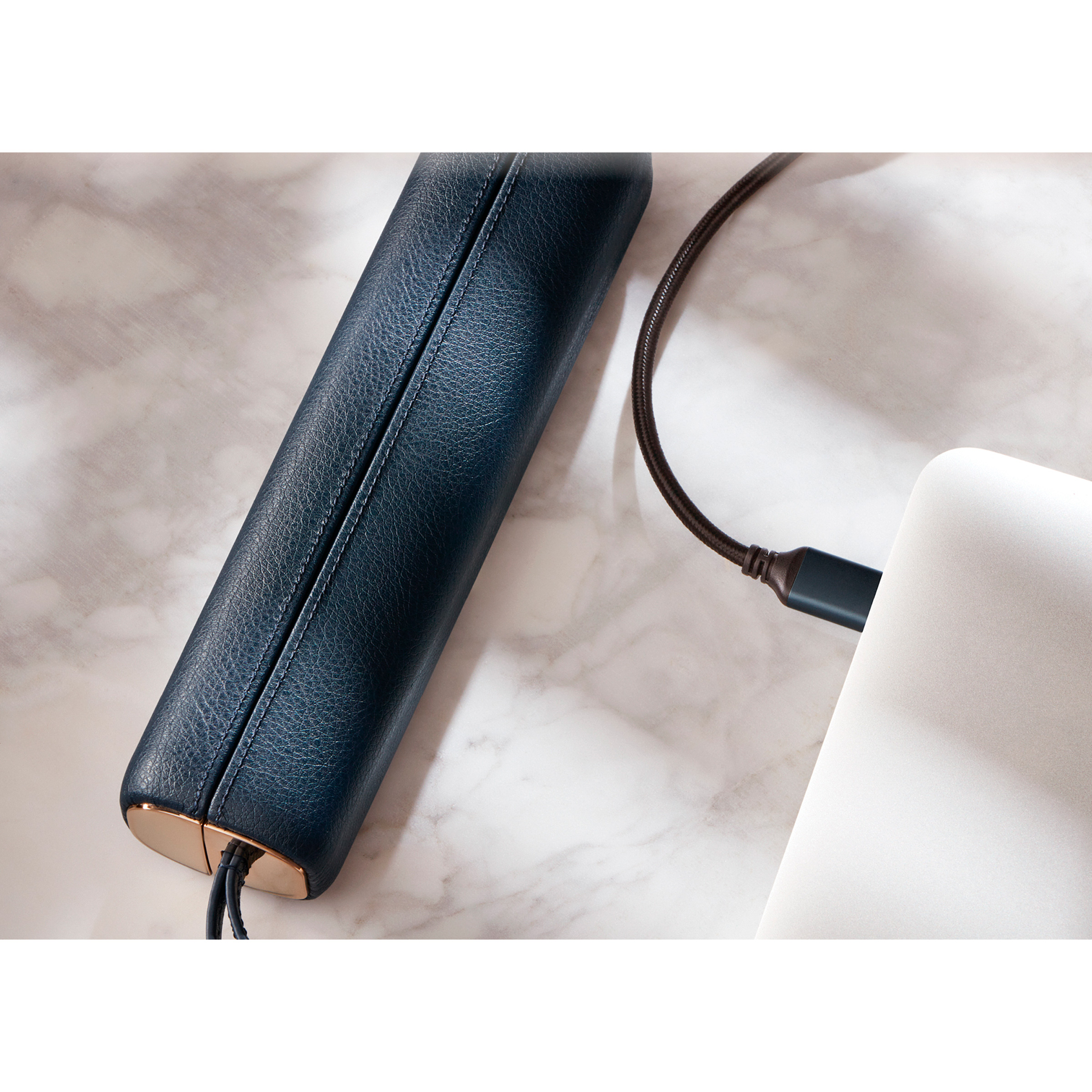 Ciemnoniebieskie skórzane urządzenie ładujące się za pomocą brązowego kabla podłączonego do laptopa.