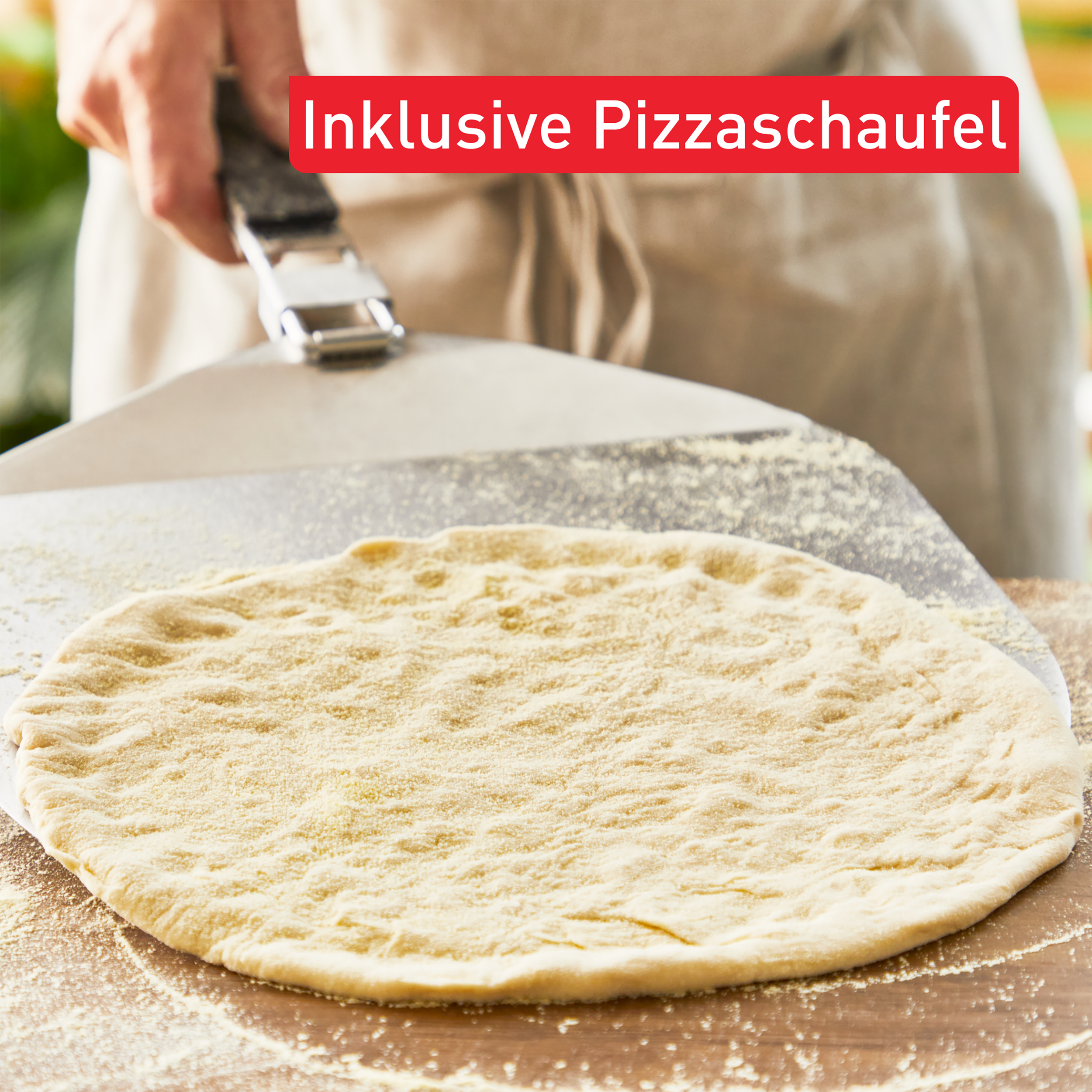 Person hält eine Pizzaschaufel mit einem Pizzaboden. Text 'Inklusive Pizzaschauefl' sichtbar.