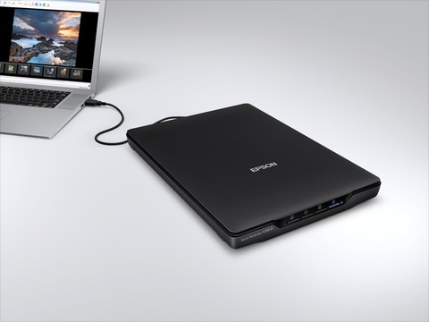 Zwarte Epson-scanner aangesloten op een laptop op een wit oppervlak.