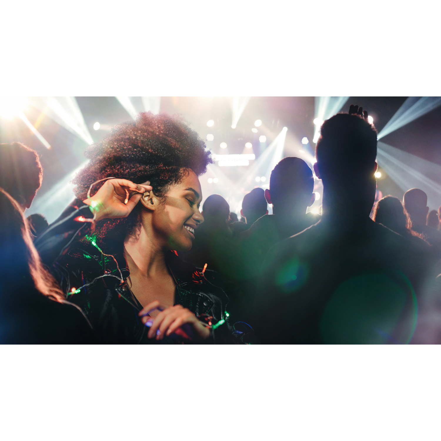 Woman in the crowd at a concert. She is smiling and wearing a jacket with lights.