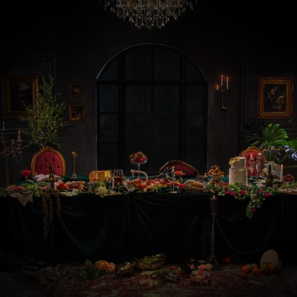 Dunkler Raum, langer Tisch mit Essen, Blumen und Kerzen gedeckt.