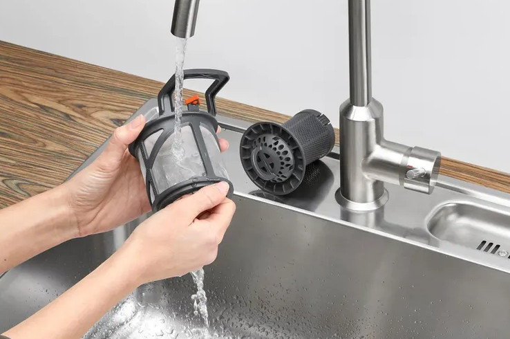 Ręce myjące filtr zmywarki pod bieżącą wodą w zlewozmywaku ze stali nierdzewnej.