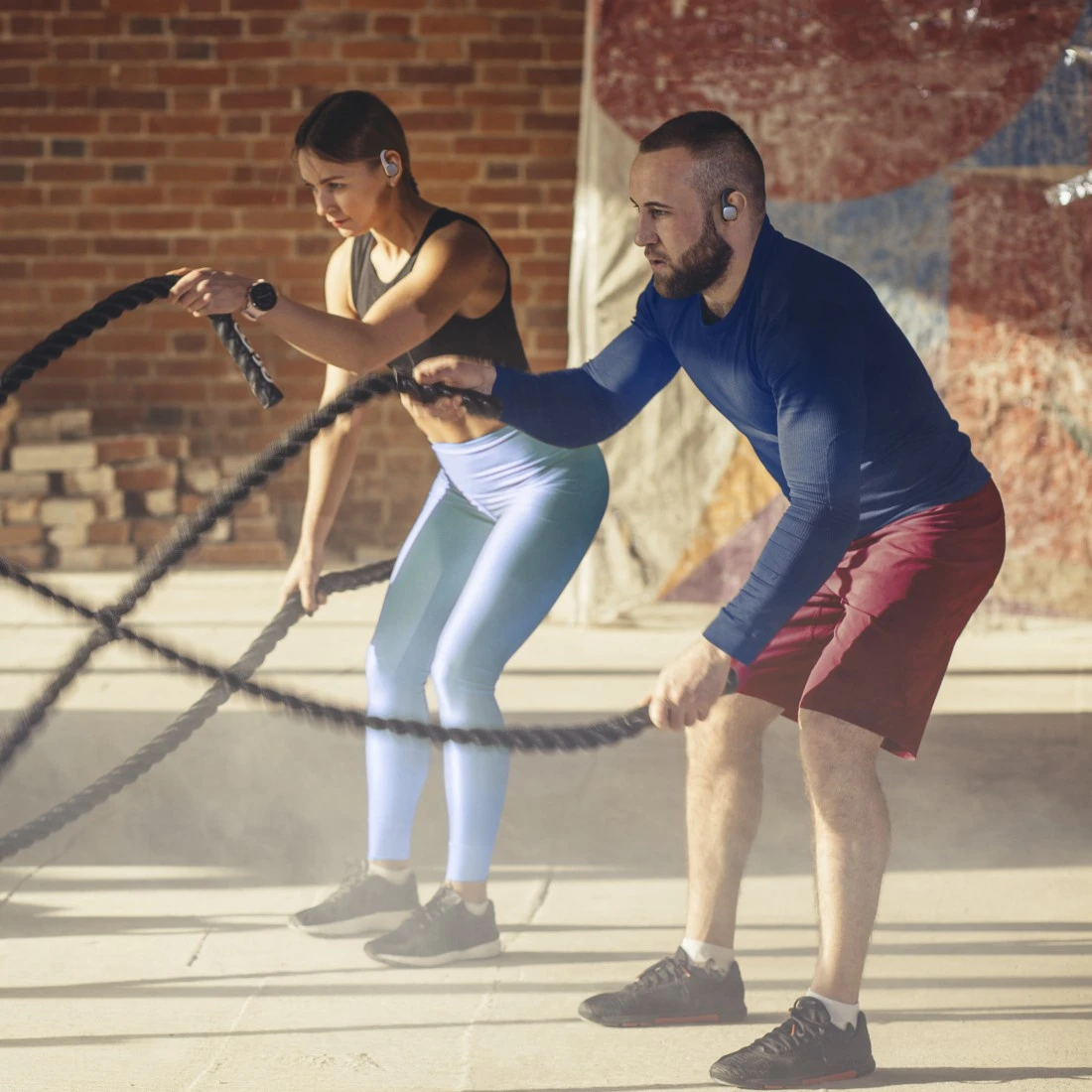 Zwei Personen trainieren mit Seilen im Fitnessstudio. Einer hat Ohrhörer.