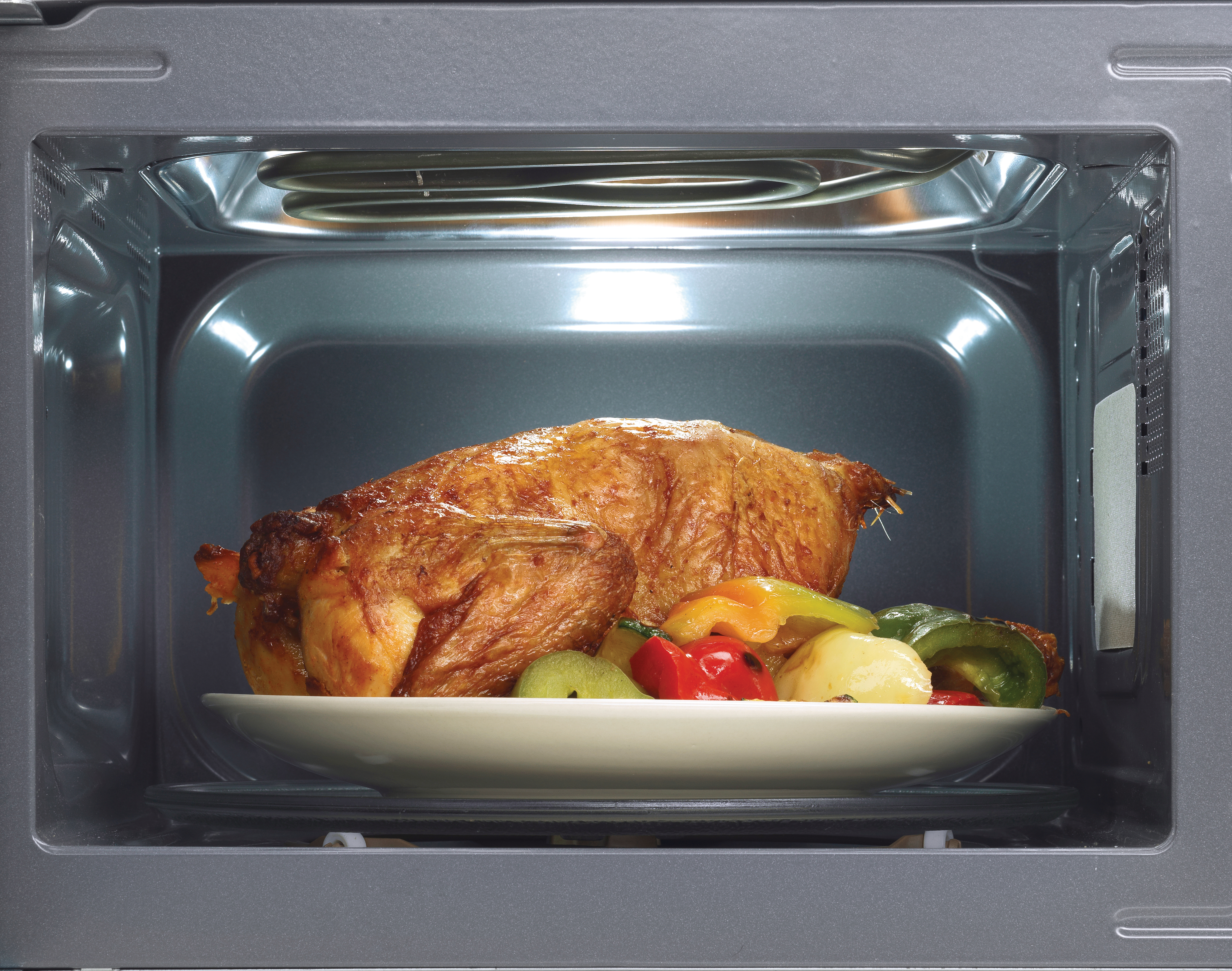 Gebratenes Hähnchen mit Gemüse auf einem Teller in einer Mikrowelle.