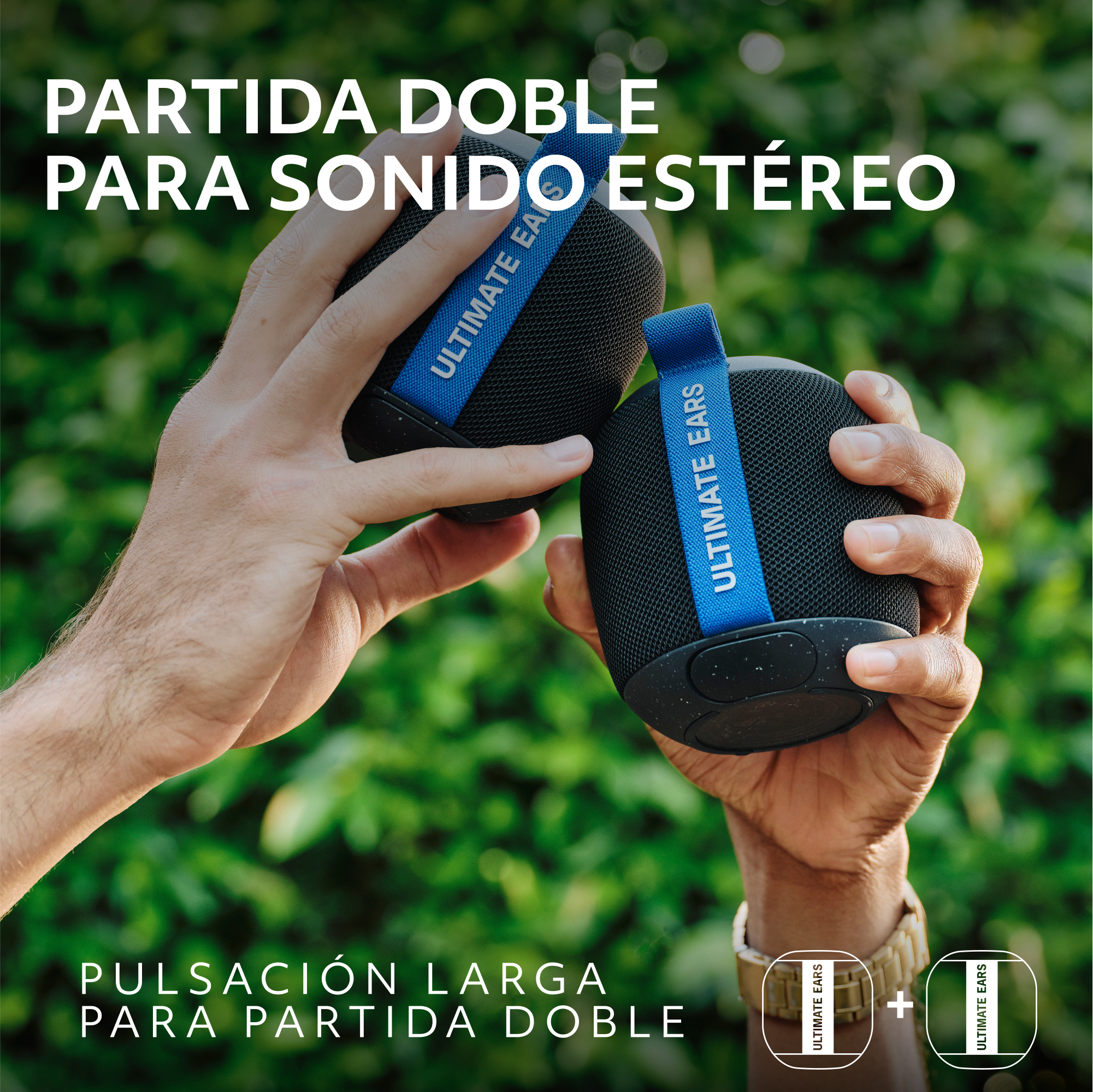 Manos sosteniendo dos altavoces negros con correas azules contra un fondo verde borroso.