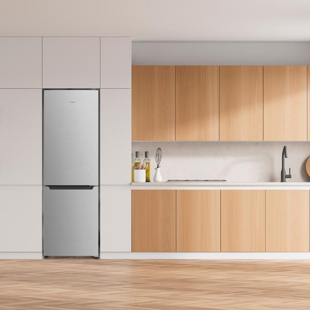 Cocina moderna con nevera plateada, armarios de madera y suelo de madera clara.