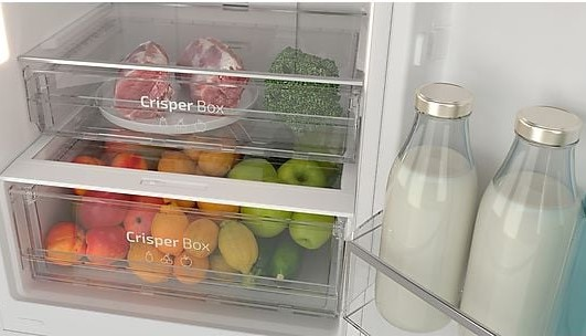 Un refrigerador con dos cajones para verduras con productos y dos botellas de leche a un lado.