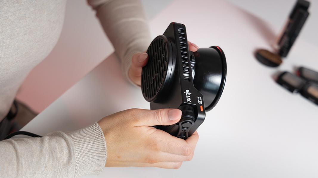 Hände halten ein schwarzes Videolicht. Das Videolicht hat einen Lüfter und einen Drehknopf.