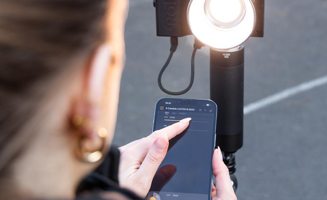 Eine Person hält ein Smartphone und stellt die Farbe eines Lichts über eine App ein. Ein Licht scheint.