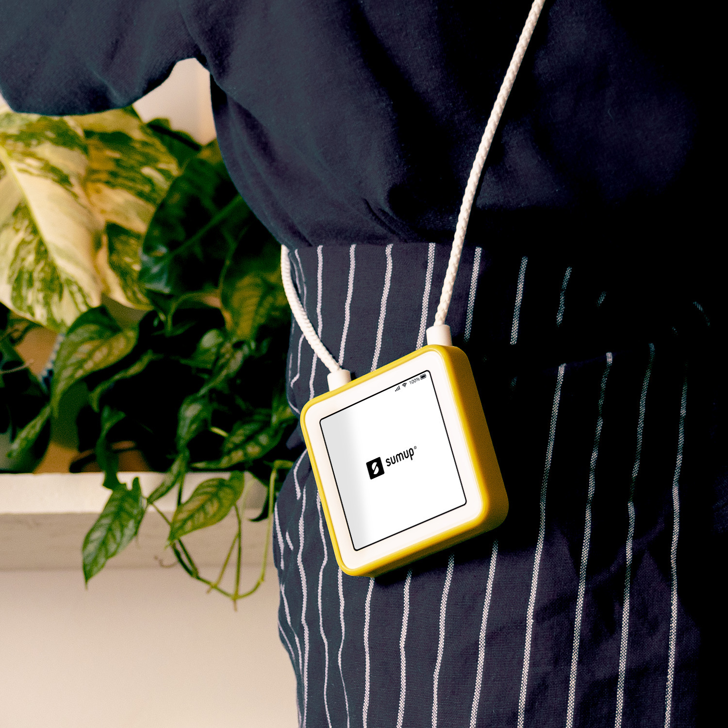 A person wearing a yellow SumUp device around their neck, against a background of plants.