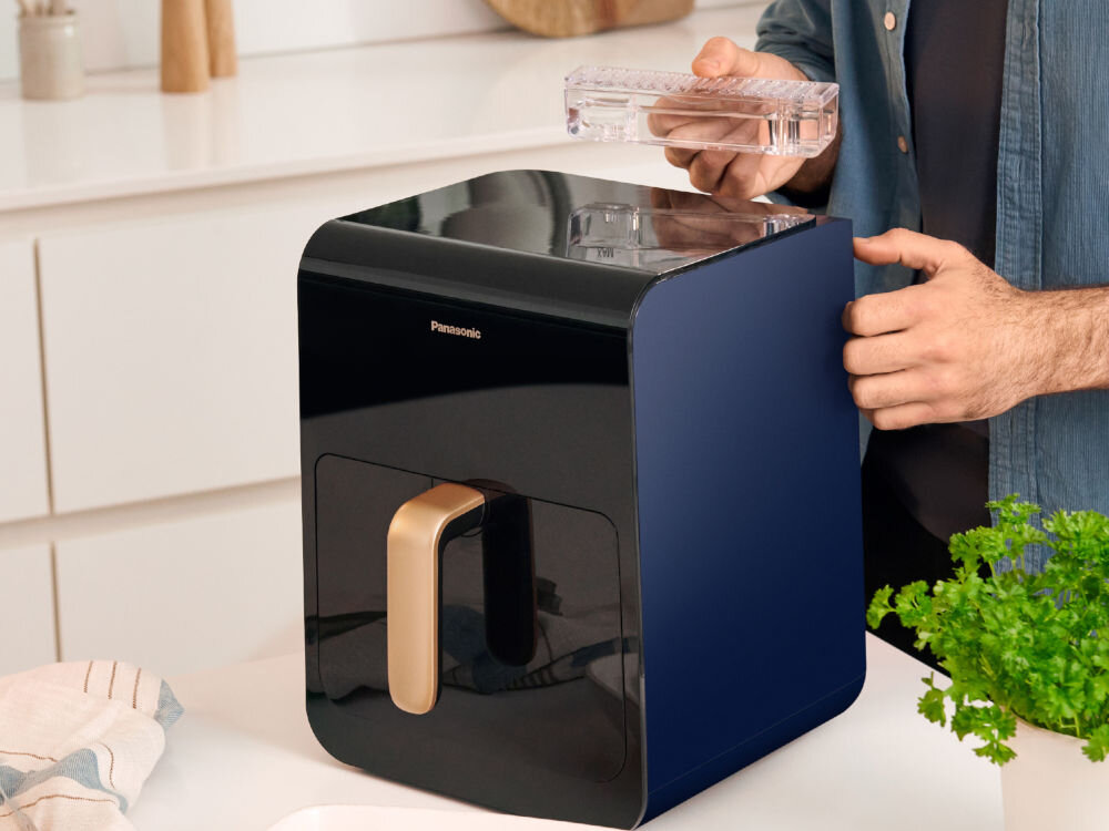 Czarna i niebieska frytkownica z złotym uchwytem. Osoba trzyma przezroczystą część.