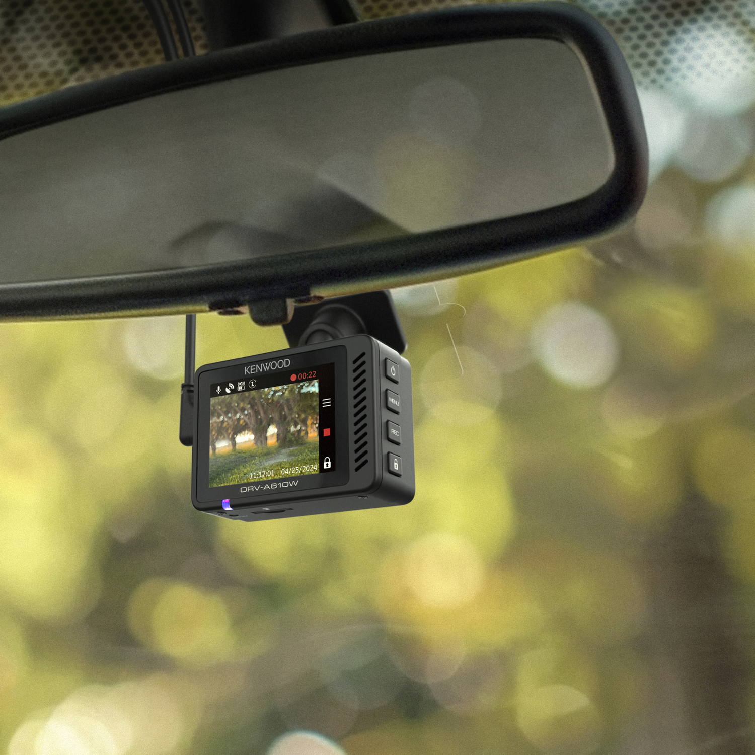 A Kenwood dashcam hangs from a car's rearview mirror, displaying a road view.