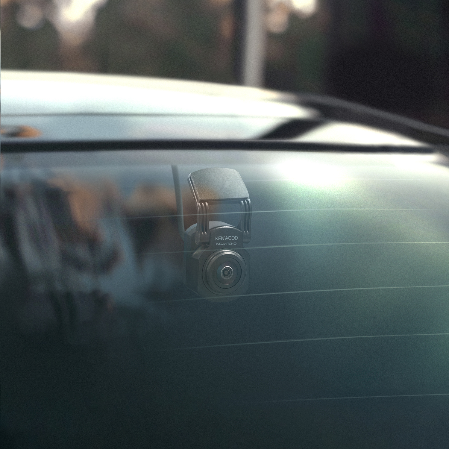 A Kenwood dashcam is mounted on a car's rear window. It has a camera and an antenna.