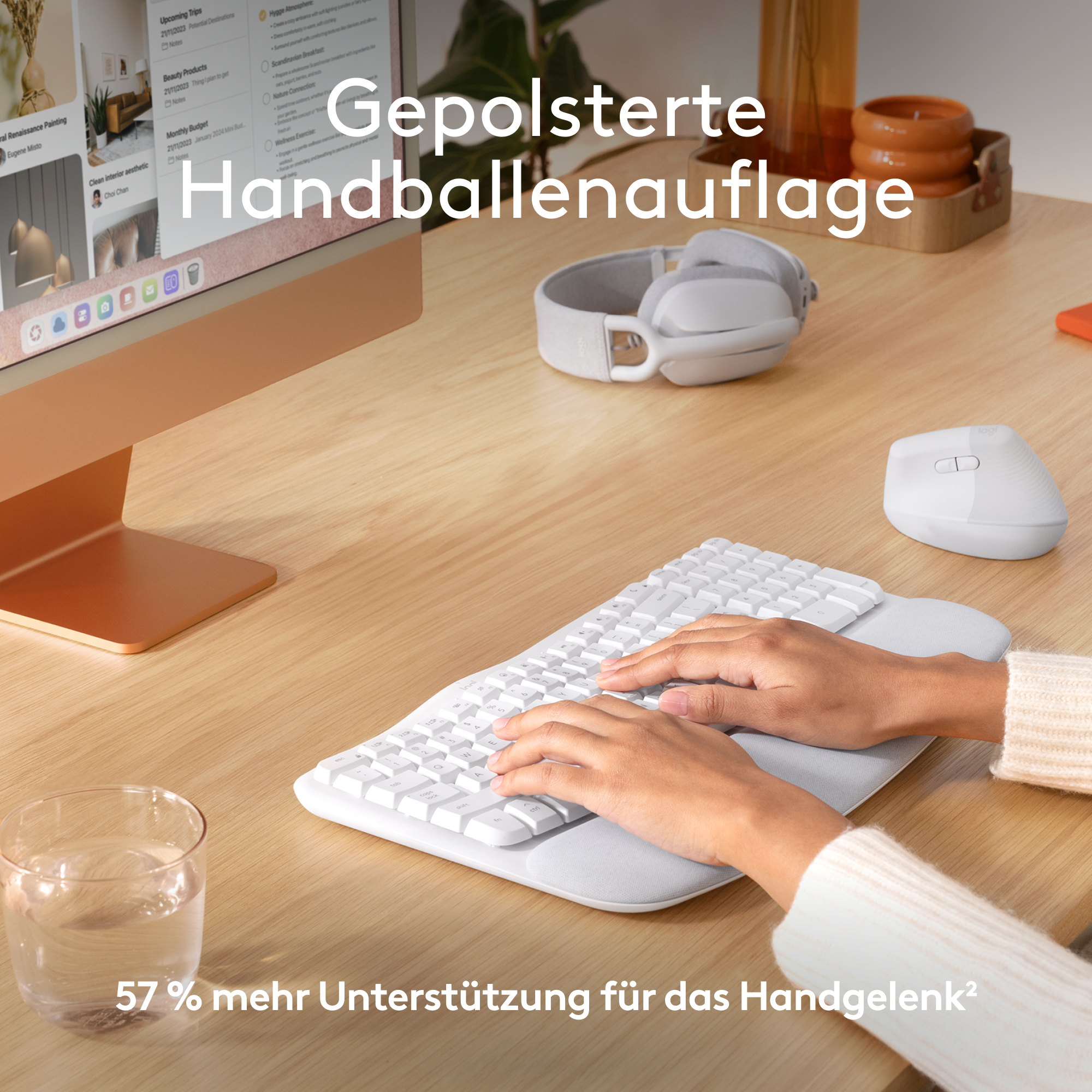 Ein Schreibtisch-Setup mit einer weißen Tastatur mit Handgelenkauflage und einem Glas Wasser.