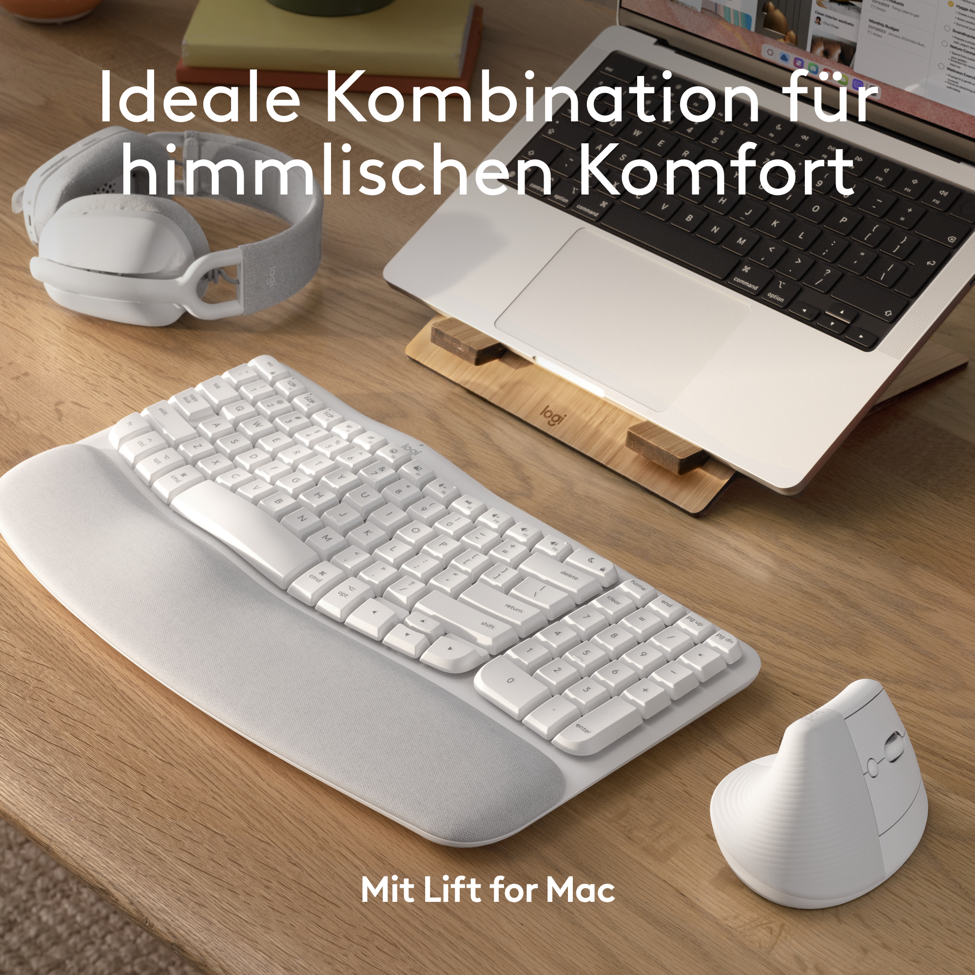 Ein weißes Tastatur- und Maus-Setup auf einem Holztisch mit Laptop und Kopfhörern.