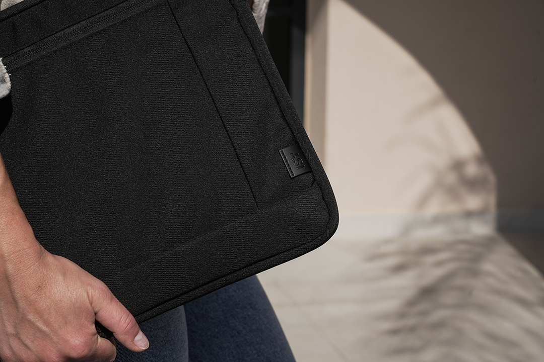 Egy személy egy fekete laptop táskát tart. A táskán egy kis logó látható.