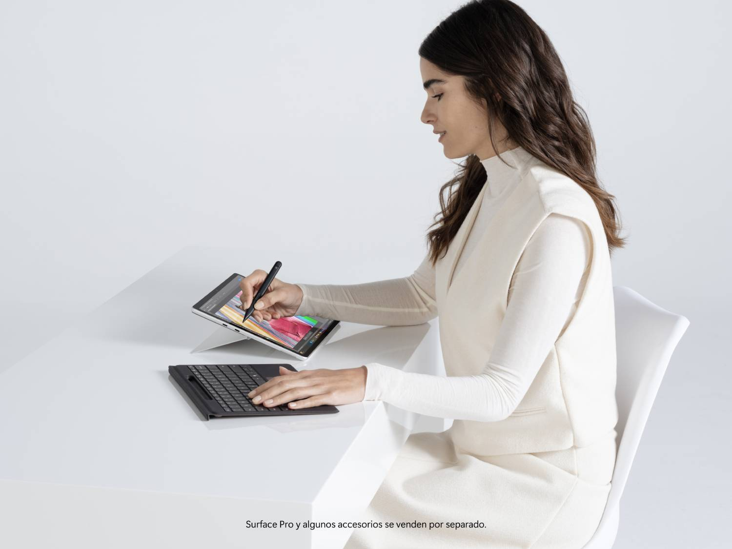 Mujer con una tableta y teclado en una mesa blanca, usando un lápiz óptico.