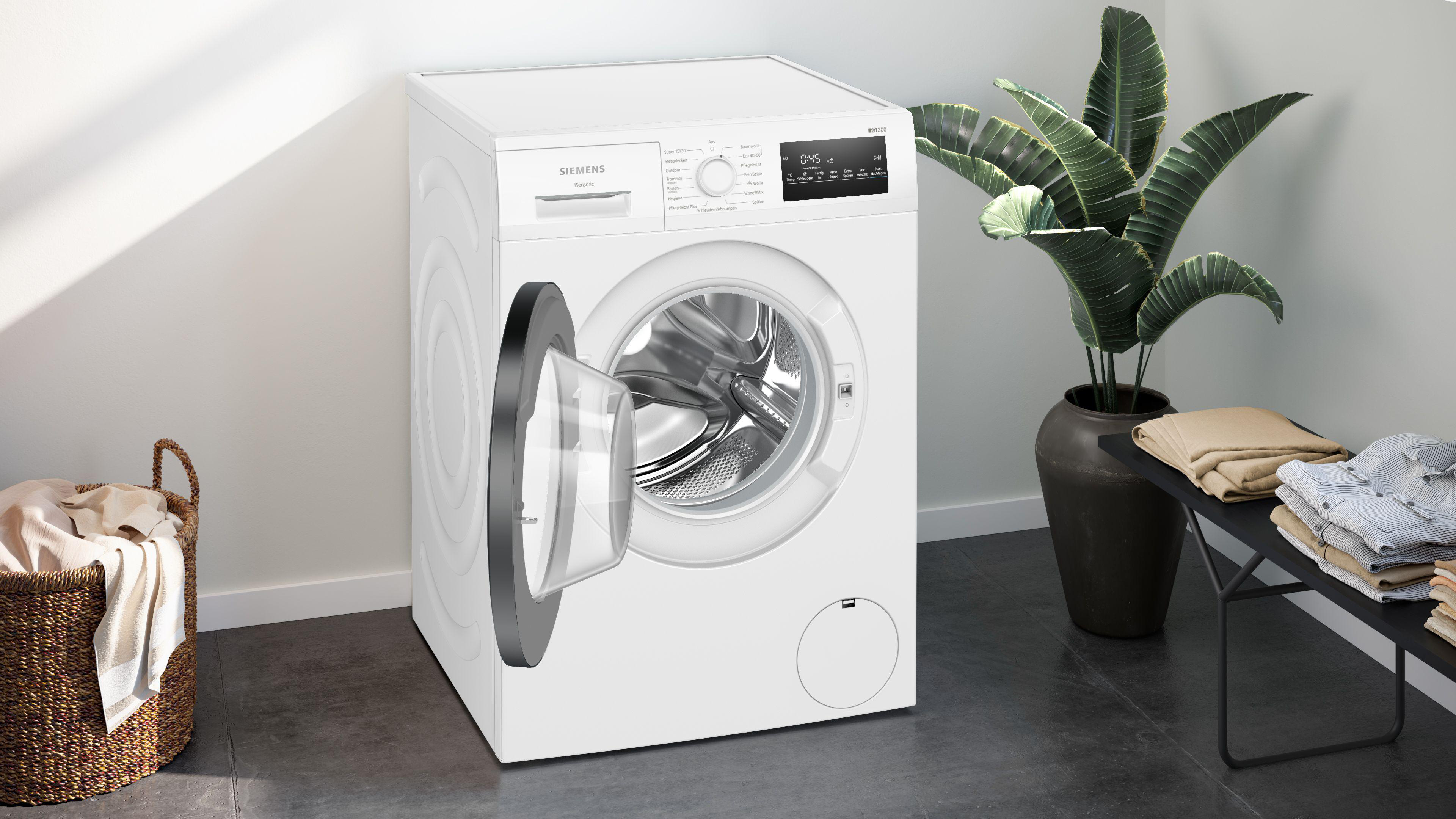Eine weiße Siemens Waschmaschine mit geöffneter Tür, neben einem Korb und Handtüchern.