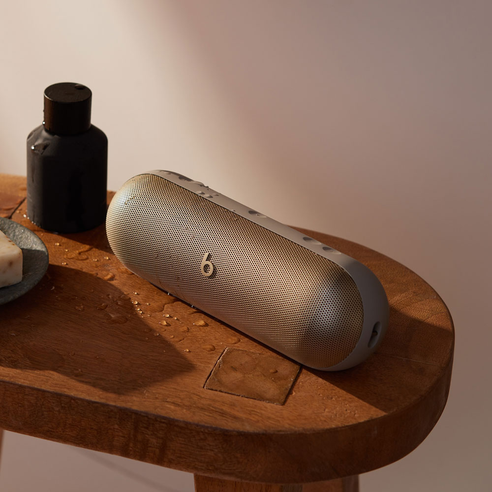 Haut-parleur Beats sur un tabouret en bois avec du savon et une bouteille noire. Des gouttes d'eau sont visibles.