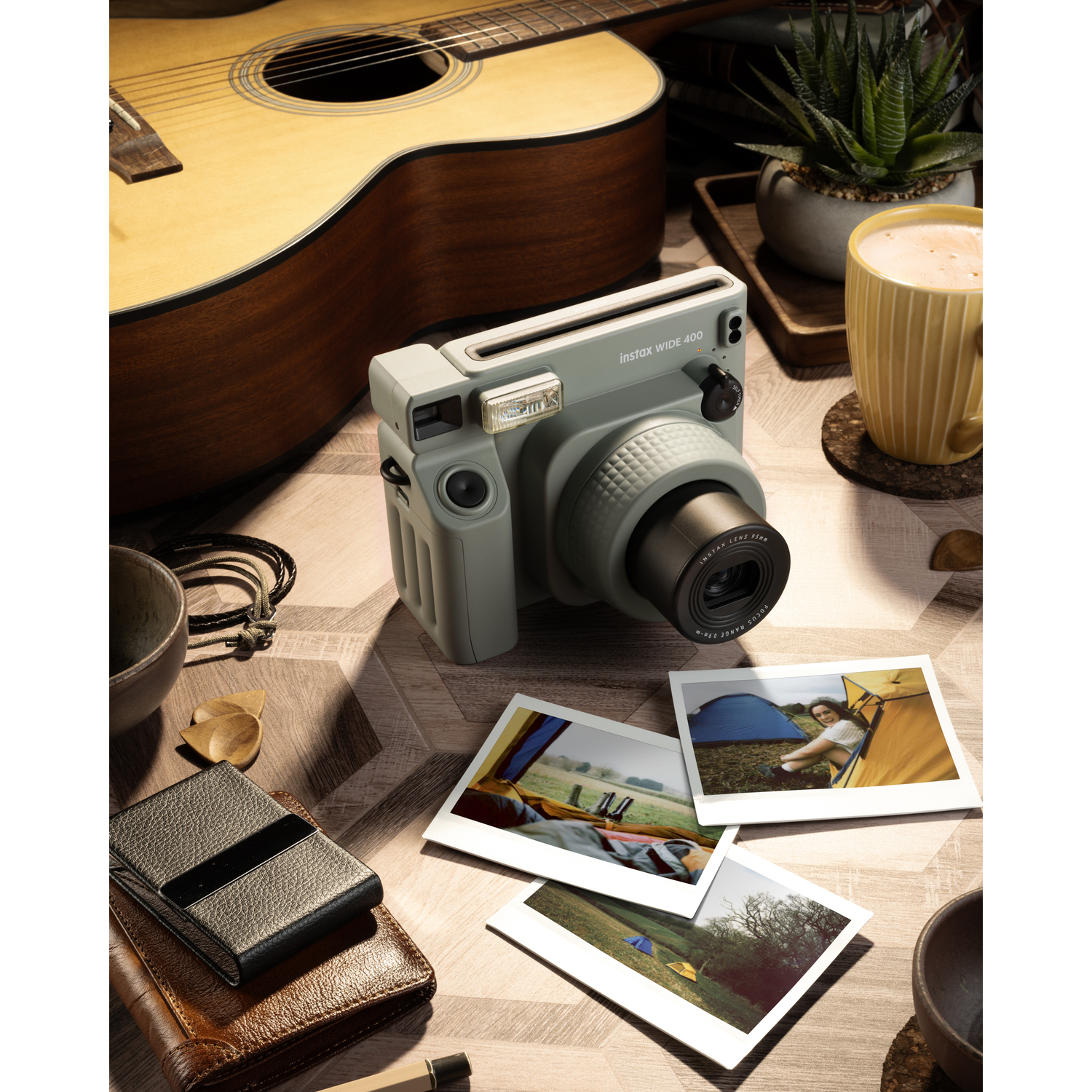 Een camera met foto's op een tafel, met een gitaar, koffie en andere items. De camera is lichtgroen.