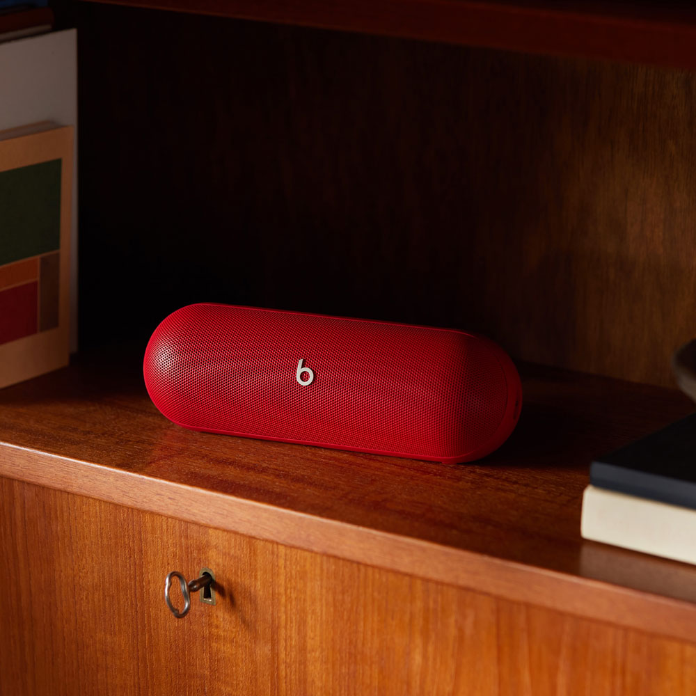 Haut-parleur Beats rouge sur un meuble en bois, livres à côté.