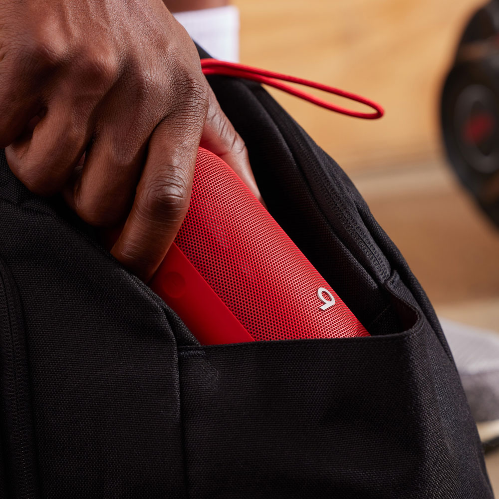 Une main mettant un haut-parleur rouge dans un sac noir.