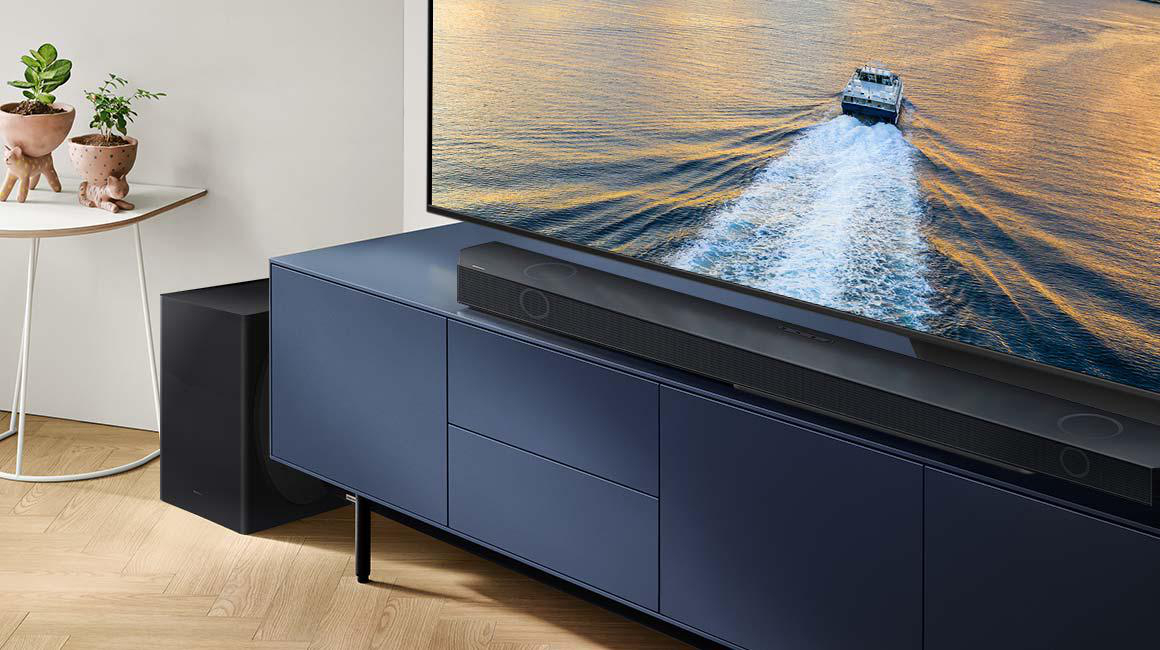Wohnzimmer-Setup mit blauem Schrank, Fernseher, Soundbar und Subwoofer; eine kleine Pflanze an der Seite.
