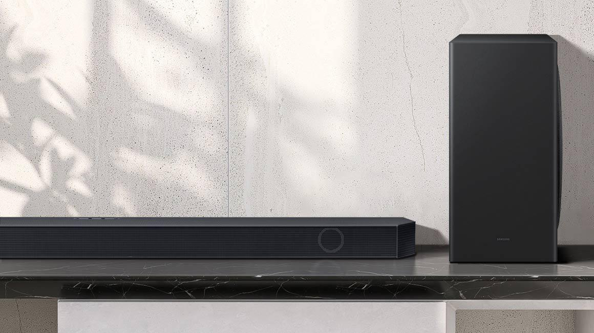 Schwarze Soundbar und Subwoofer auf Marmoroberfläche, weißer Wandhintergrund.