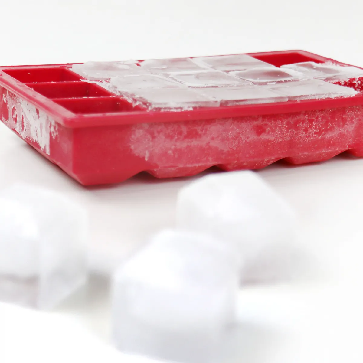 Bandeja roja para cubitos de hielo con cubitos y 3 sueltos sobre una superficie blanca.