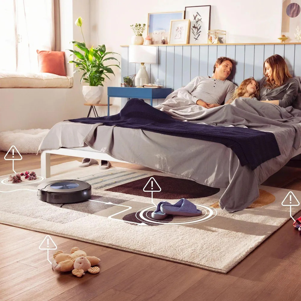 Rodzina w łóżku, robot sprząta dywan. Ostrzeżenia na przedmiotach.