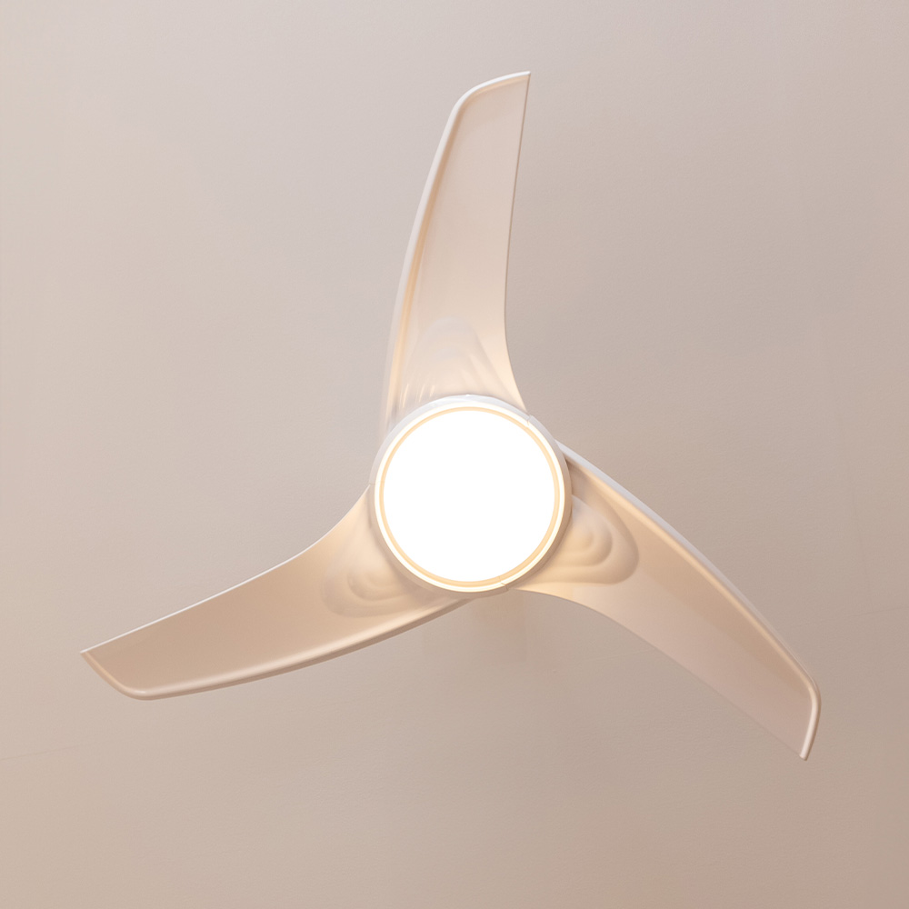 Ventilador de techo con tres aspas, luminaria en el centro. Las aspas son blancas, fondo beige claro.