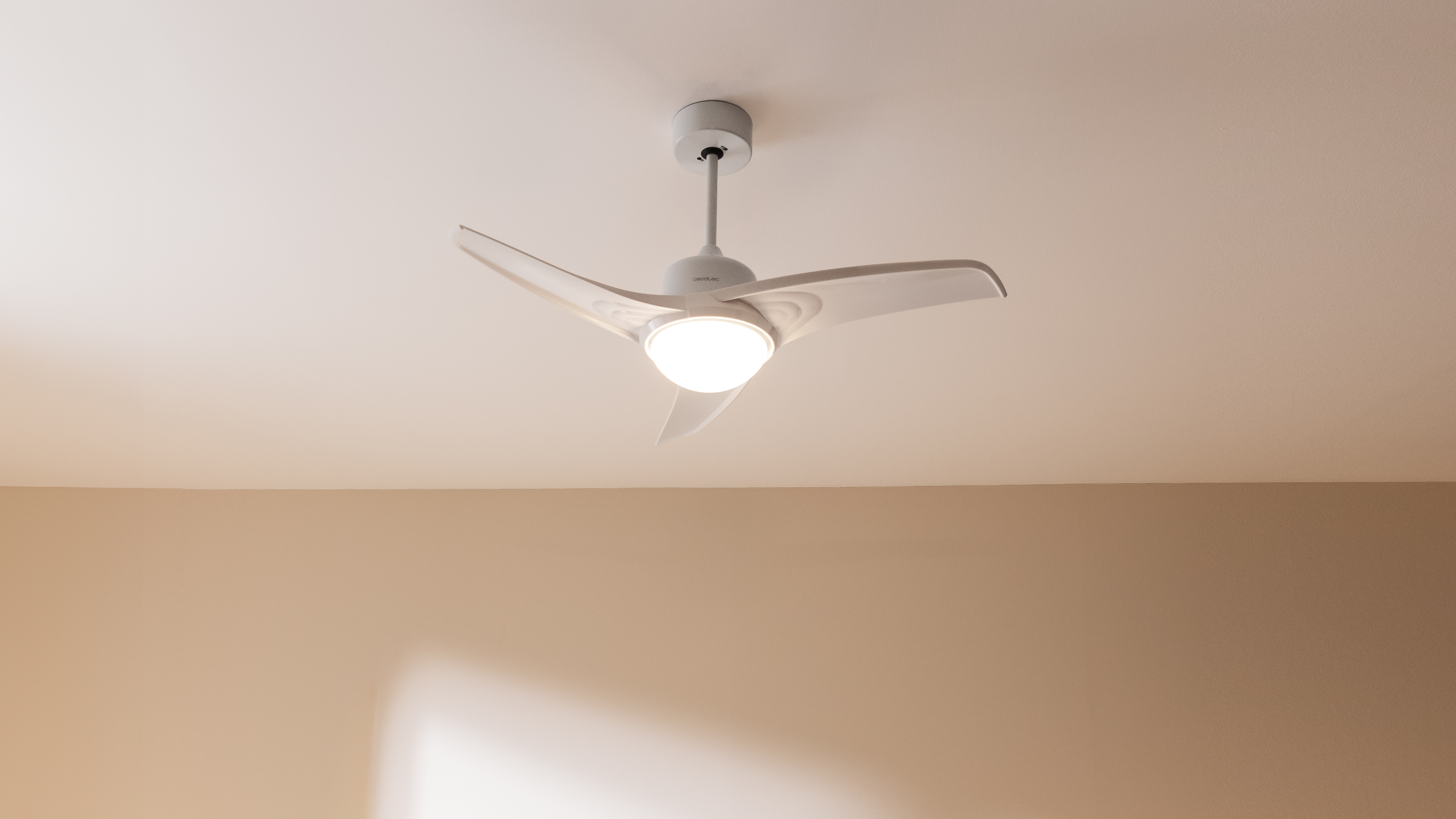 Ventilador de techo blanco con tres aspas y una luz central, montado en un techo beige.