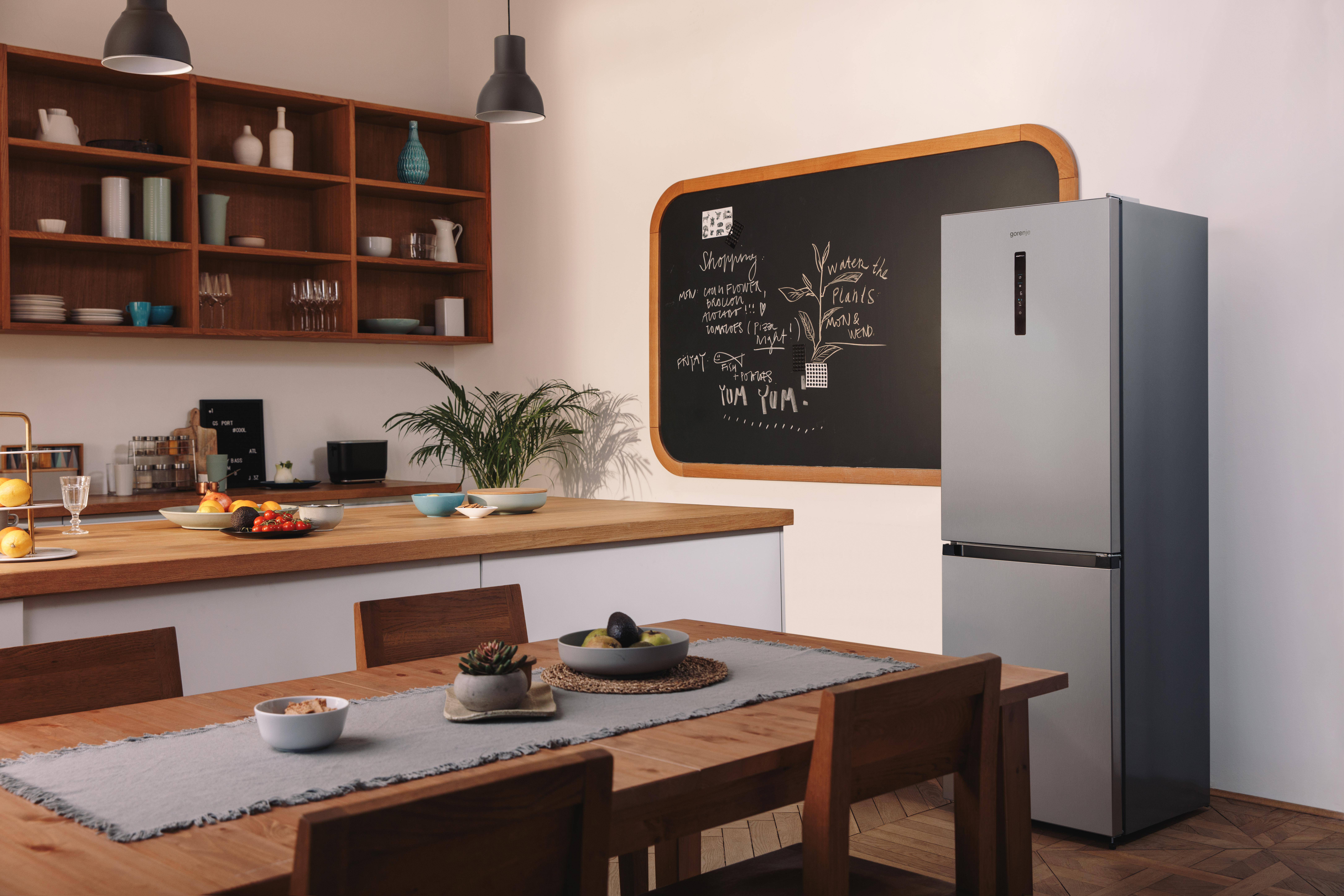 Küche mit Tisch, Kühlschrank und einer Tafel mit einer Liste. Holzregale.