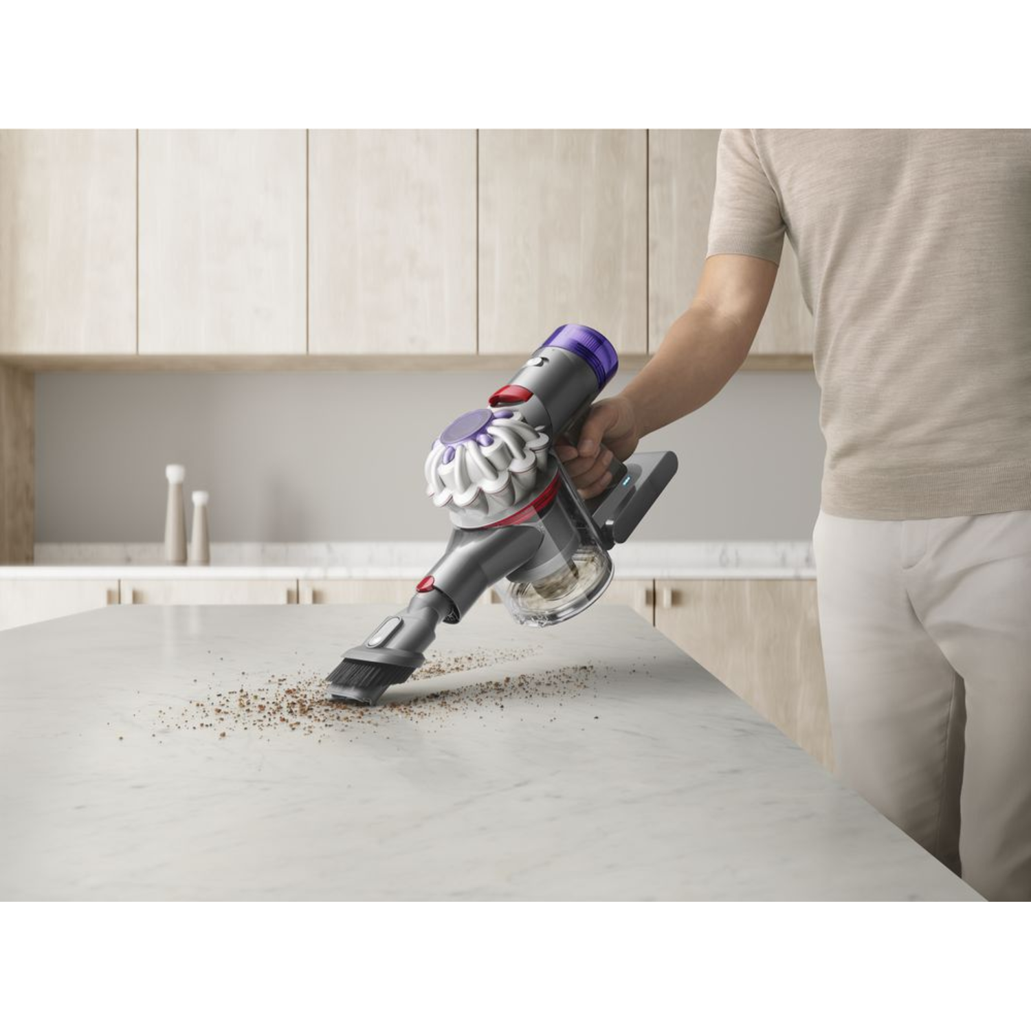Een persoon die een oppervlak stofzuigt met een grijze en paarse Dyson-stofzuiger.