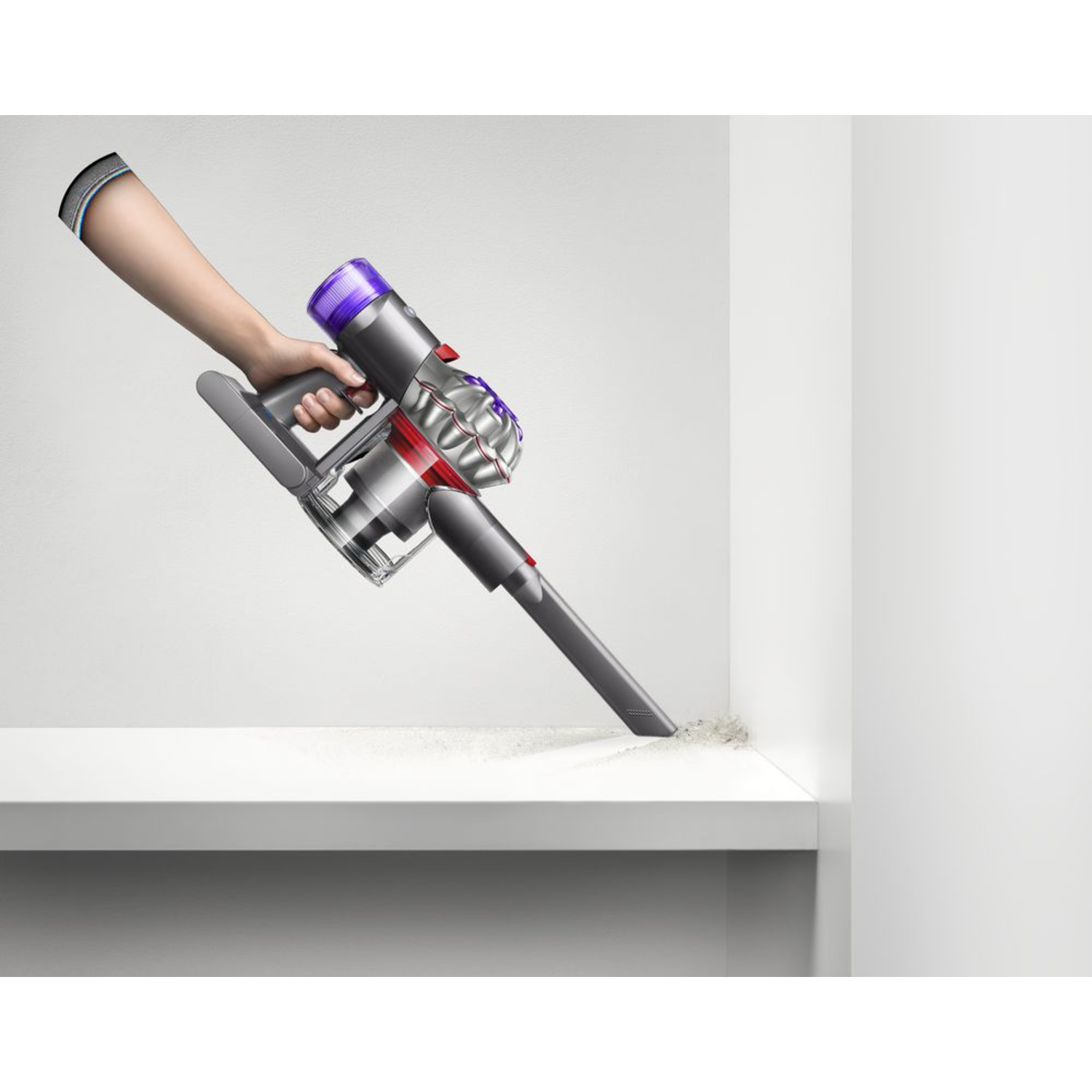 Een hand die een zilveren en paarse Dyson stofzuiger gebruikt op een witte plank.