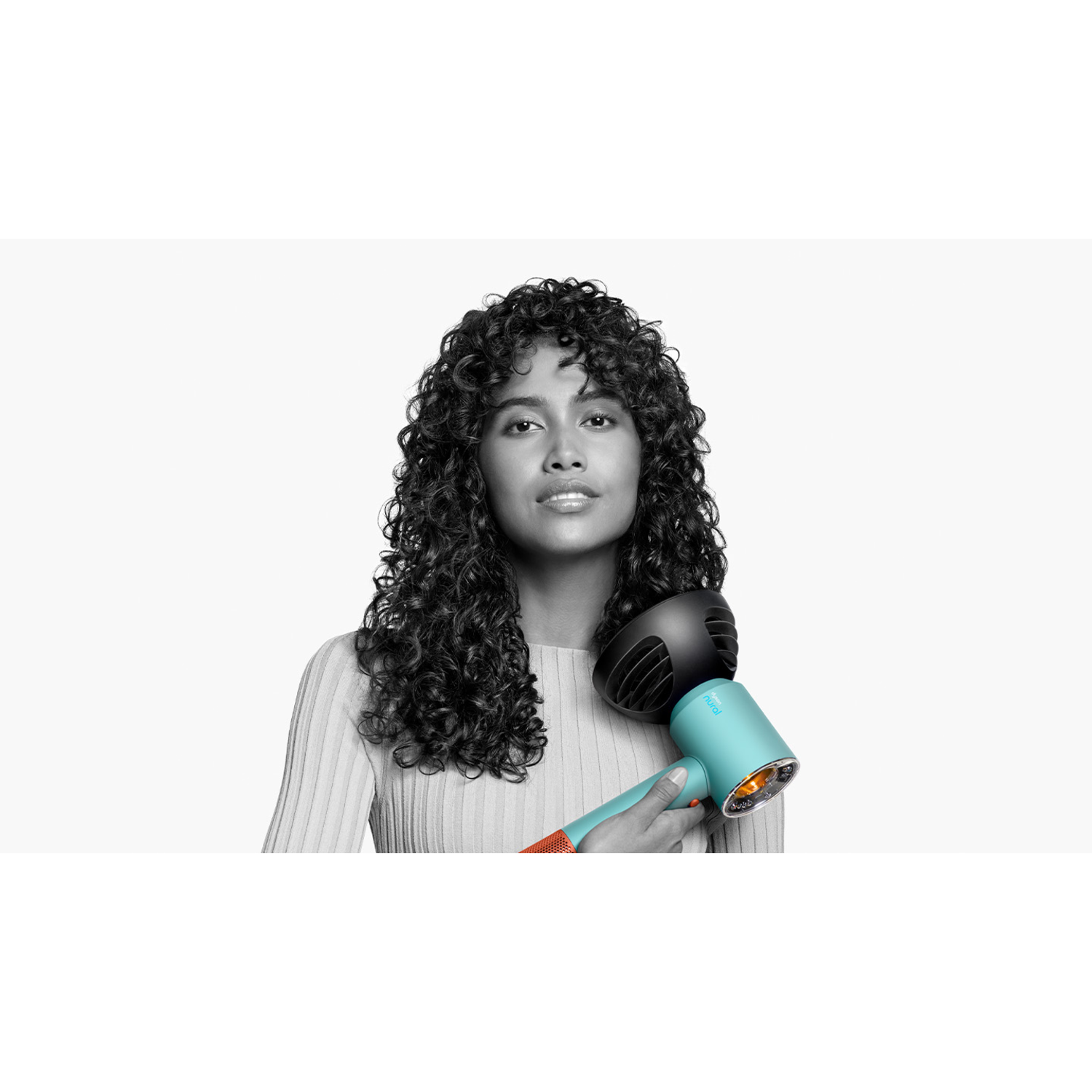 Een vrouw met krullend haar die een turquoise en zwarte föhn vasthoudt, op wit.