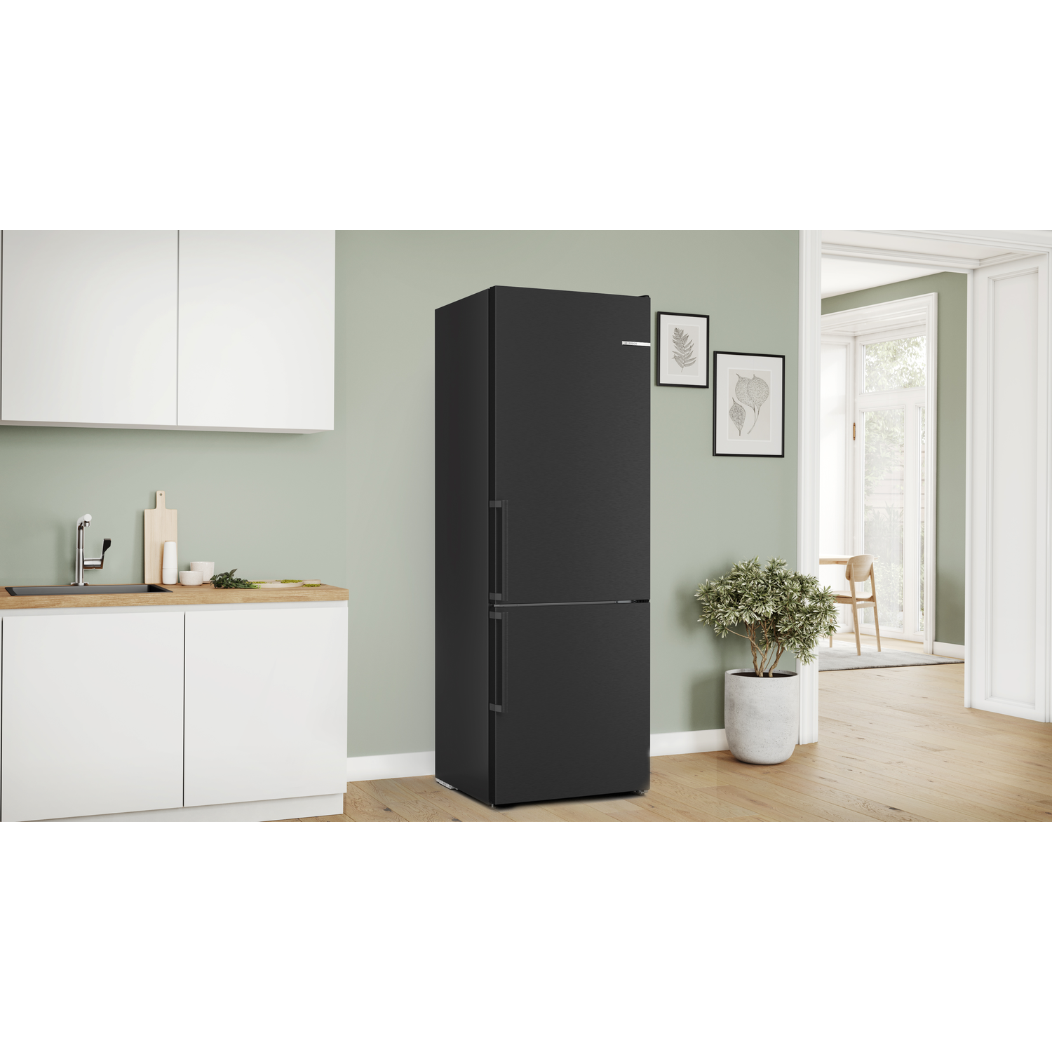 A black refrigerator in a kitchen. A plant, two pictures, and a sink are visible.