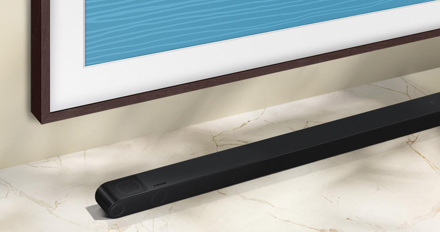 Eine schwarze Soundbar unter einem gerahmten Kunstwerk. Die Soundbar steht auf Marmor.