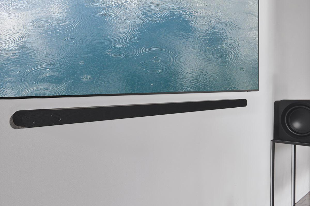 Ein Fernseher an einer weißen Wand mit einer Soundbar und einem Subwoofer darunter.