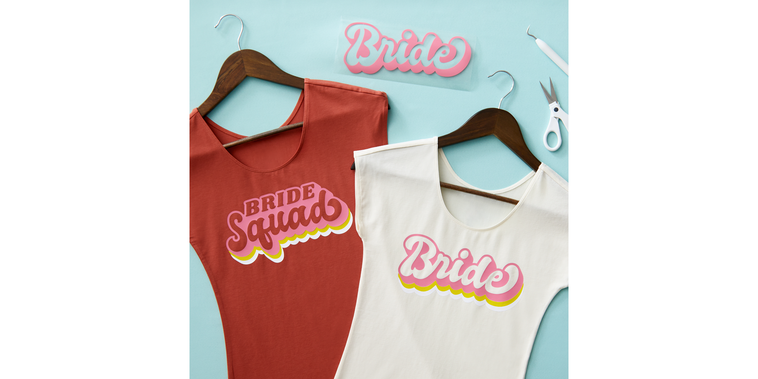 Zwei T-Shirts auf Bügeln. Rotes liest 'BRIDE SQUAD', weißes sagt 'Bride' in Pink und Gelb.