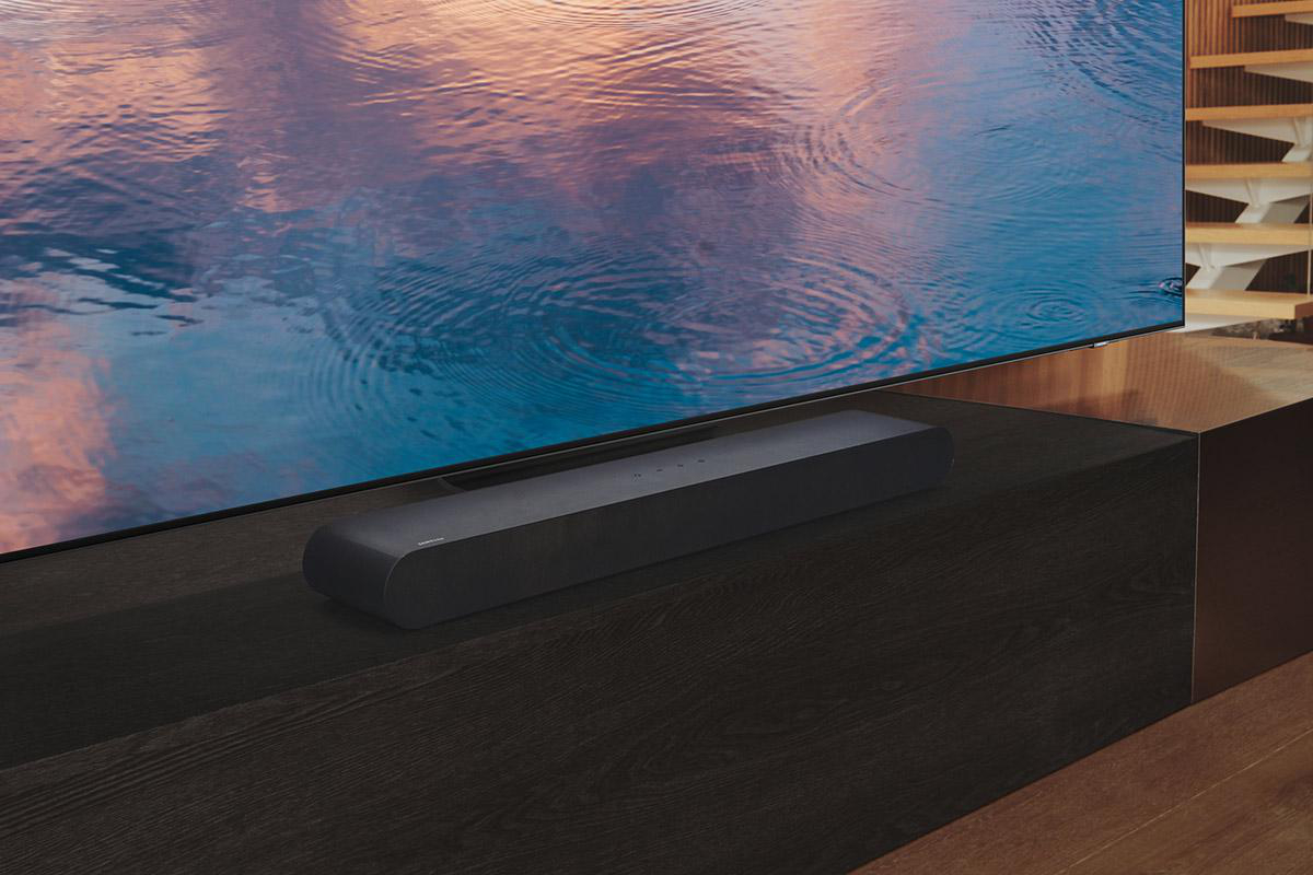Schwarze Soundbar vor einem großen Fernseher mit verschwommener Wasserszene.