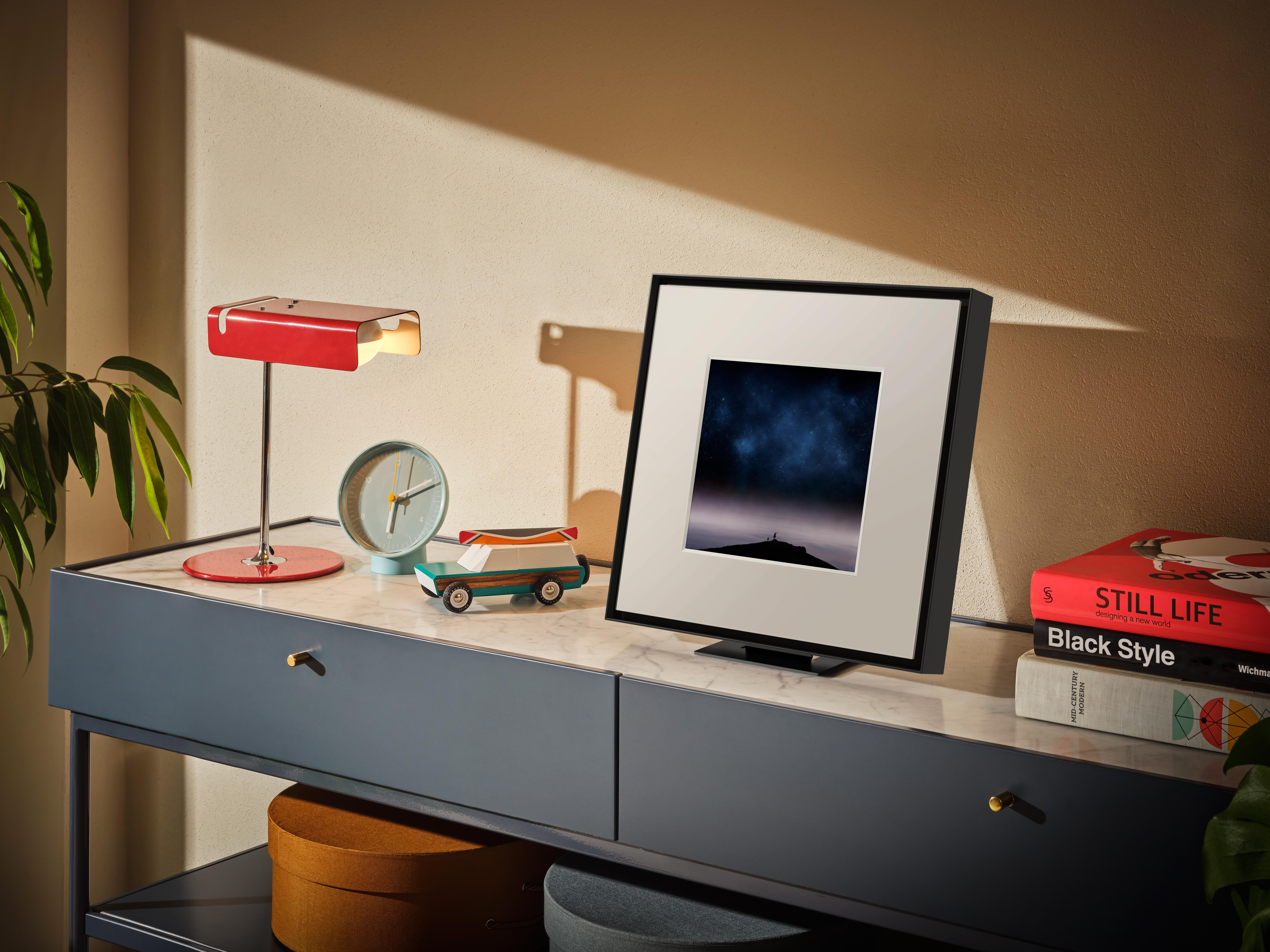 Rote Schreibtischlampe, Uhr, Spielzeugauto und gerahmtes Bild auf einem Schrank.