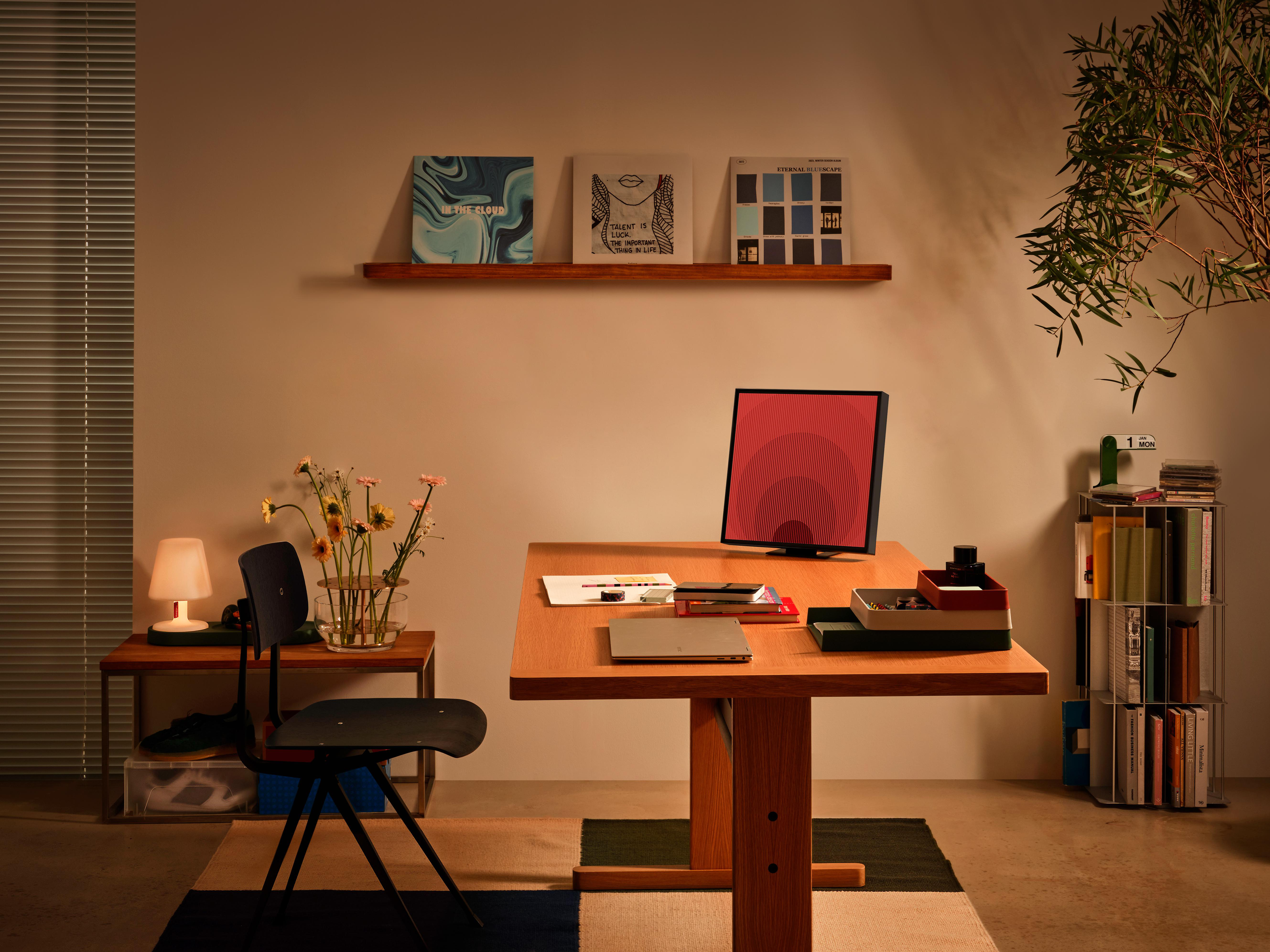 Home-Office-Szene mit Schreibtisch, Monitor, Schreibtischlampe und Dekoartikeln, Tageslicht.