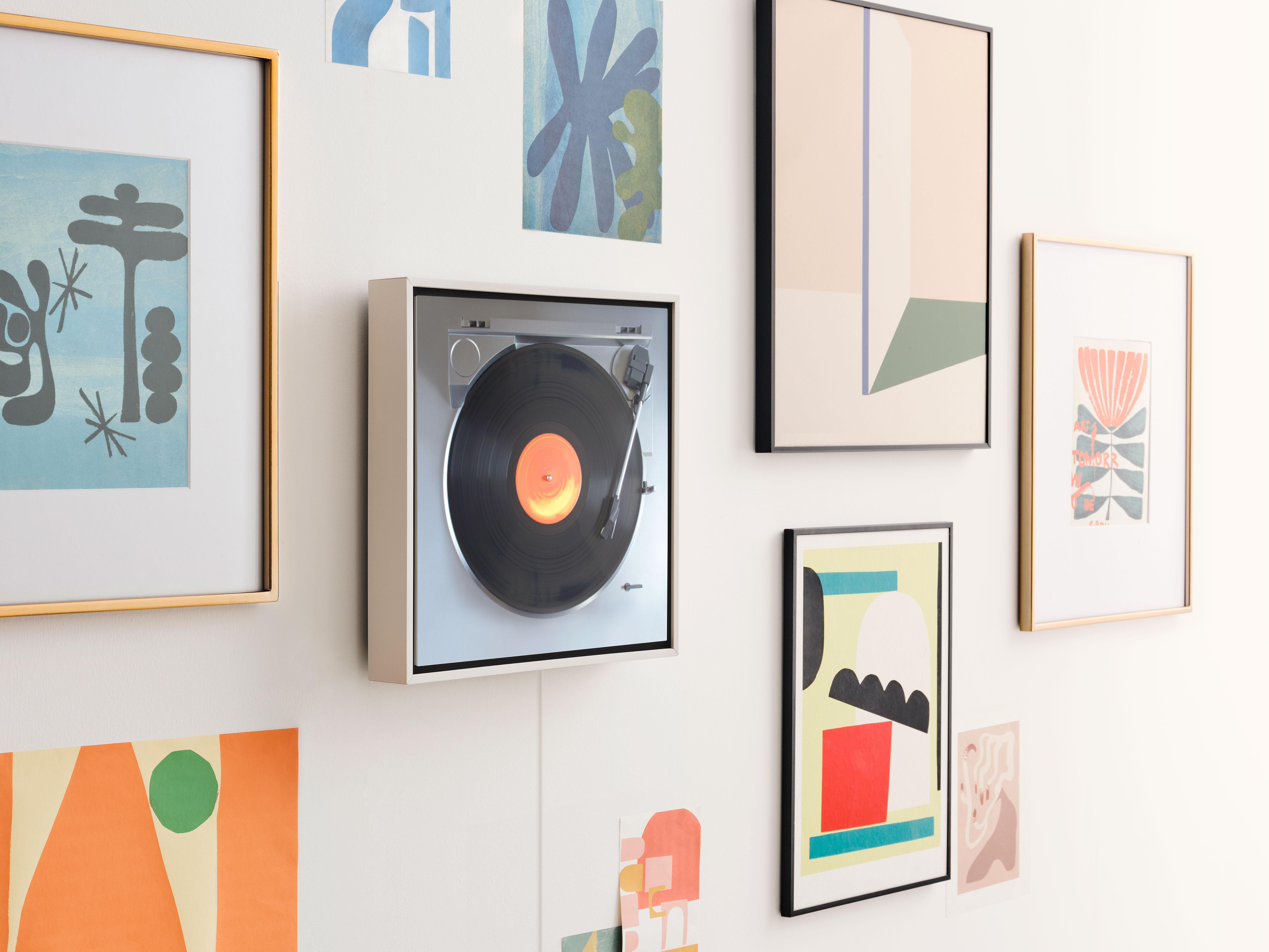 Ein Plattenspieler an einer Wand, umgeben von gerahmten Kunstwerken und farbenfrohen Drucken.
