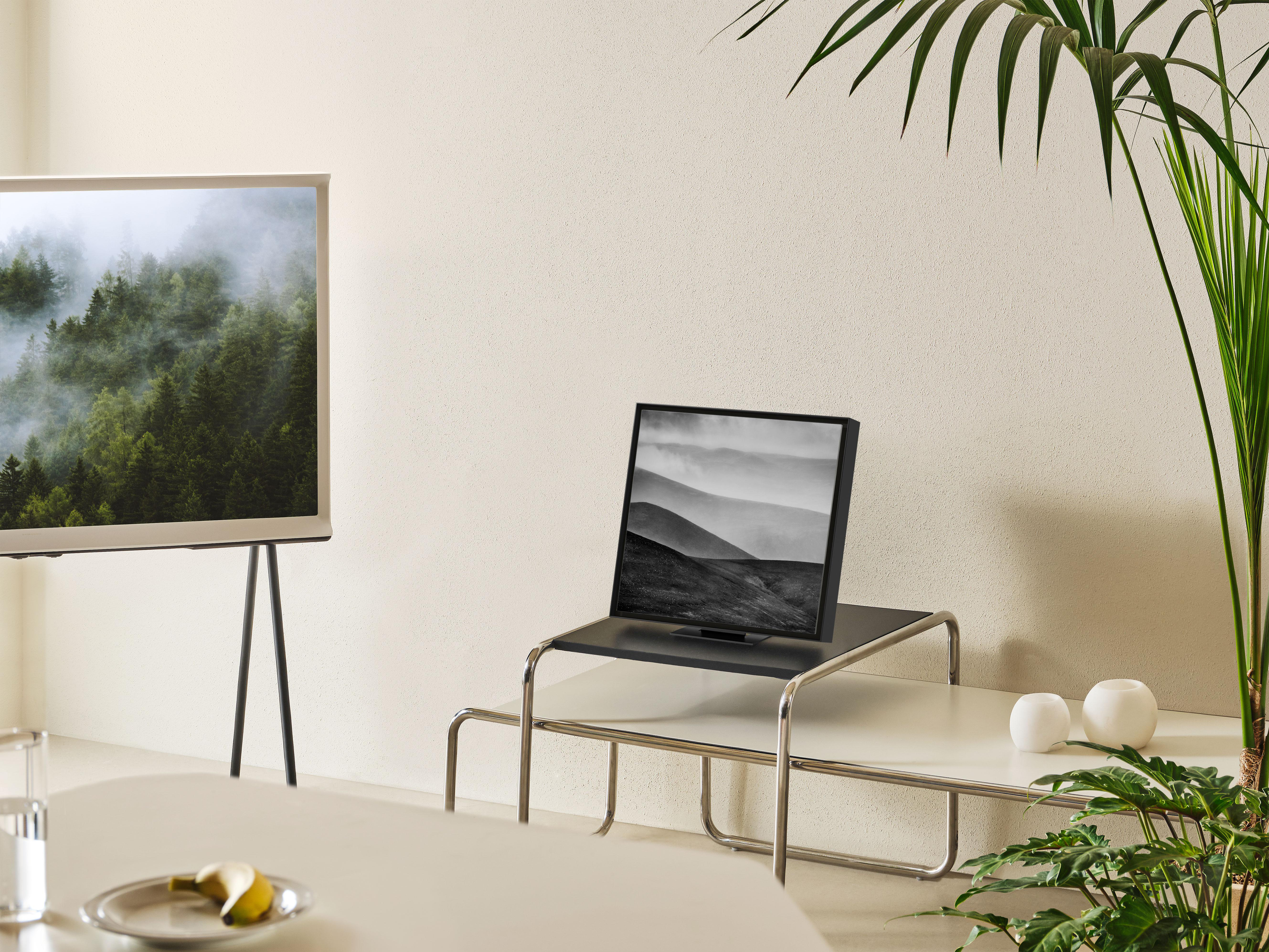 Ein modernes Wohnzimmer mit Fernseher auf Ständer, Pflanze, weißem Tisch und Stühlen.