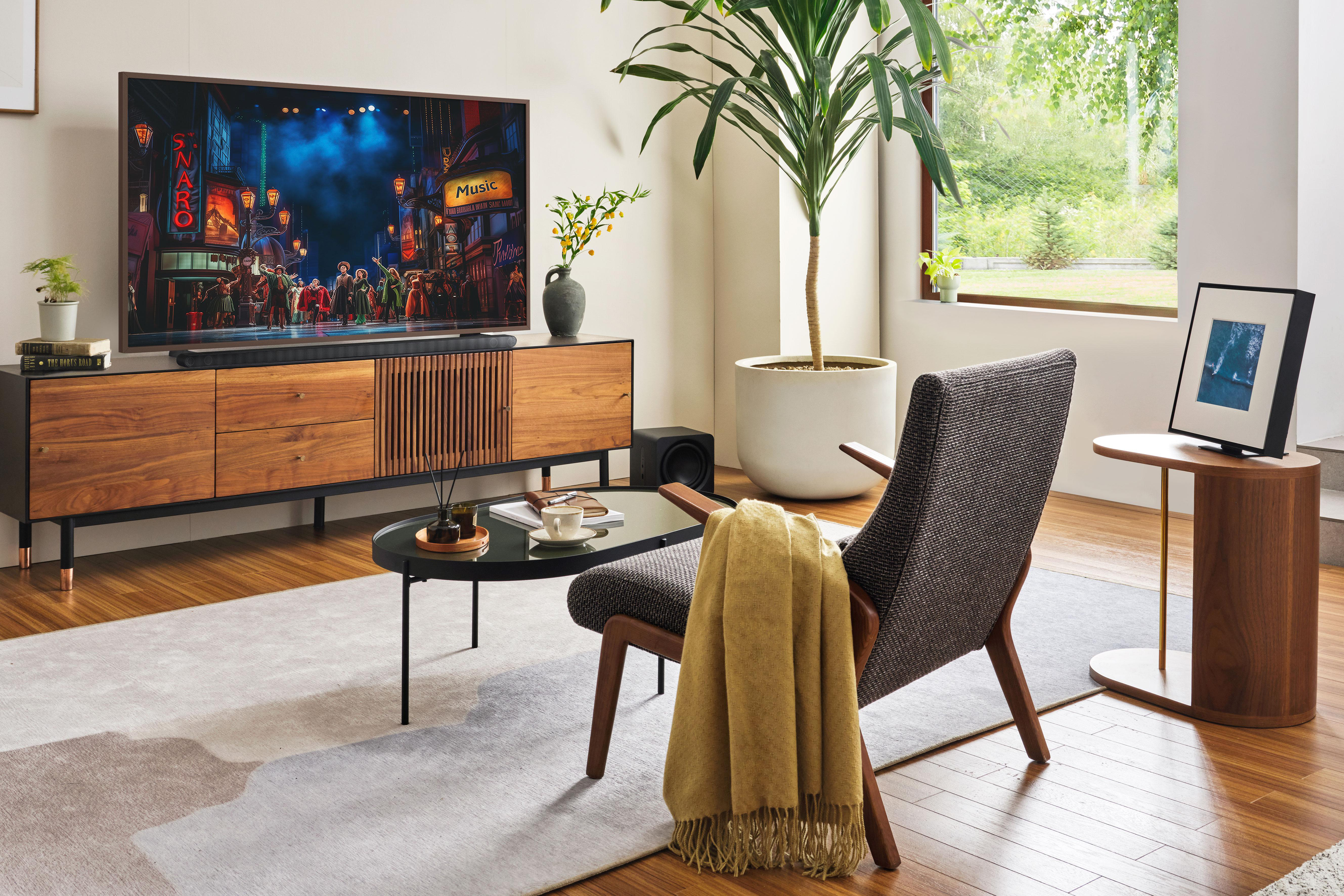 Wohnzimmer mit Fernseher, der eine Bühne zeigt, einem Stuhl, einem Couchtisch und einer Pflanze.